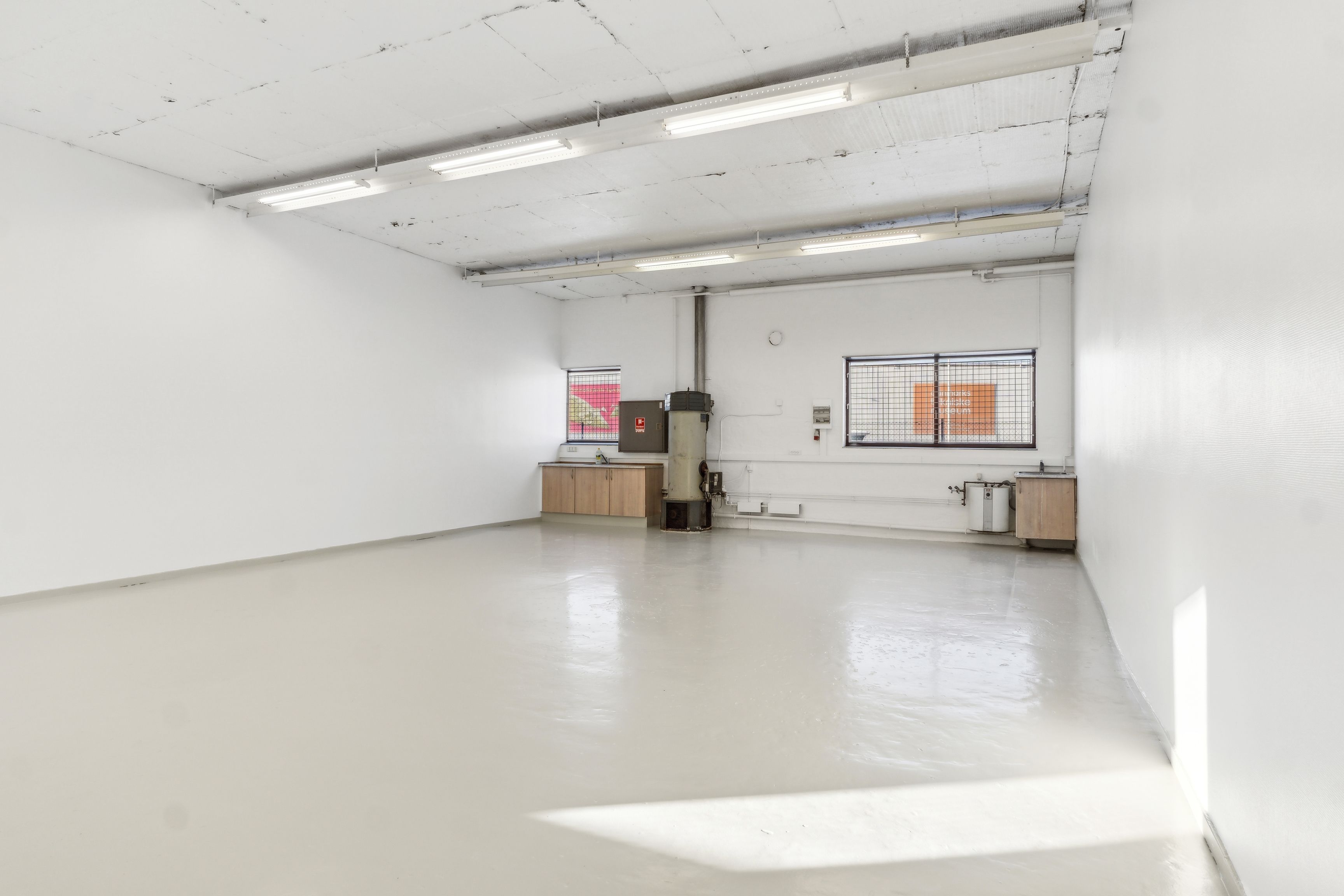 To tomme og hvide lokaler med store vinduer og lys på loftet, der reflekterer på gulvet