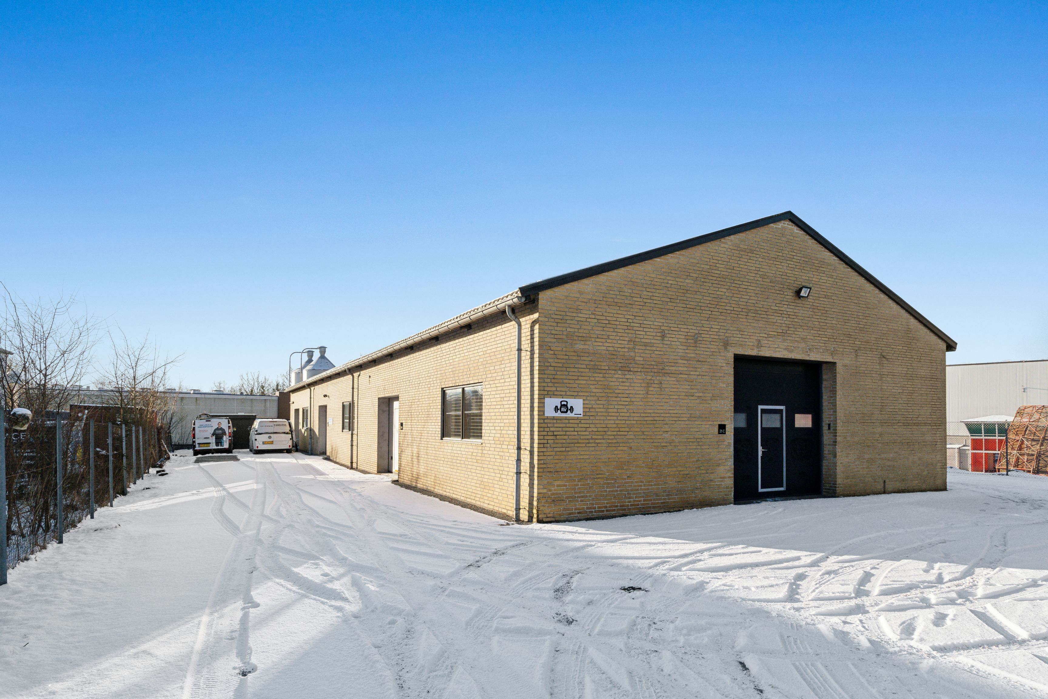 To hvide varevogn, der står parkeret udenfor et gult murstenshus, med sne på jorden og et rødt tag på bygningen i baggrunden