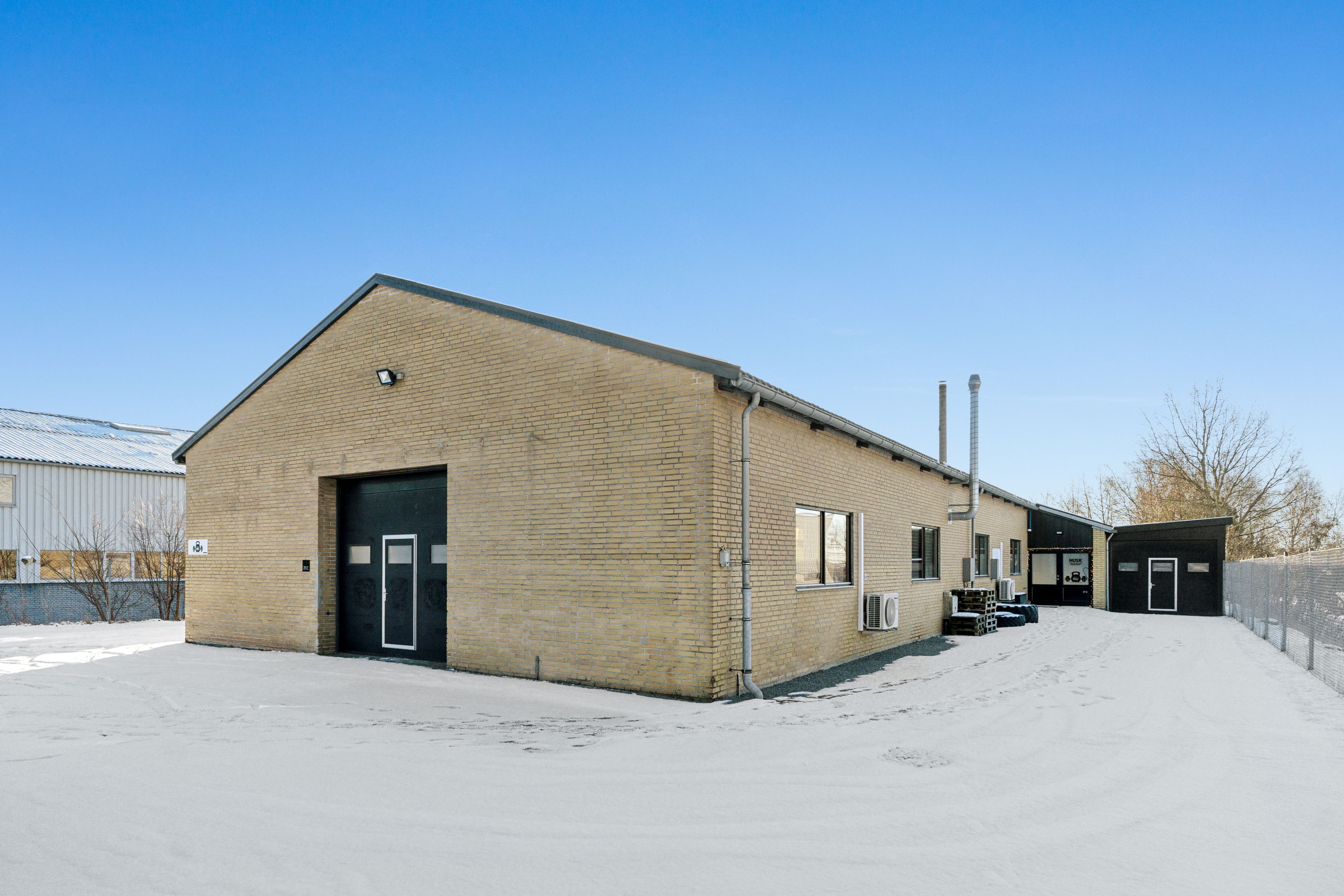 Et stort gult bygningsværk med flere indgange og en skorsten og luftkonditioneringsenhede i en snelagt have med en række af