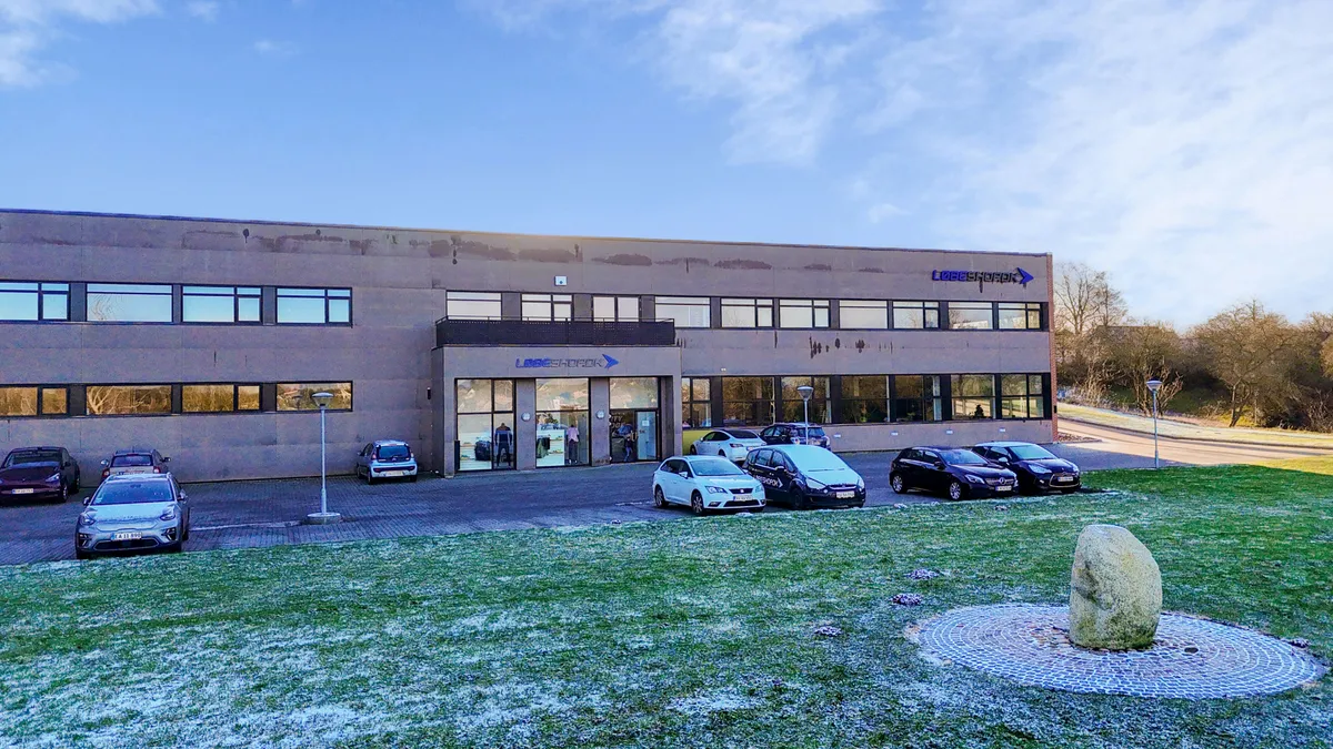 Kontorbygning med biler parkeret og græsplads med sten foran bygningen i et frosset landsted