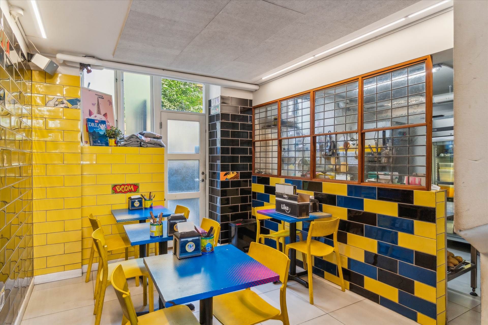 Lejlighed i café med gule og blå vægge, lysegul gulv og bord med stol, og en dør med glas.
