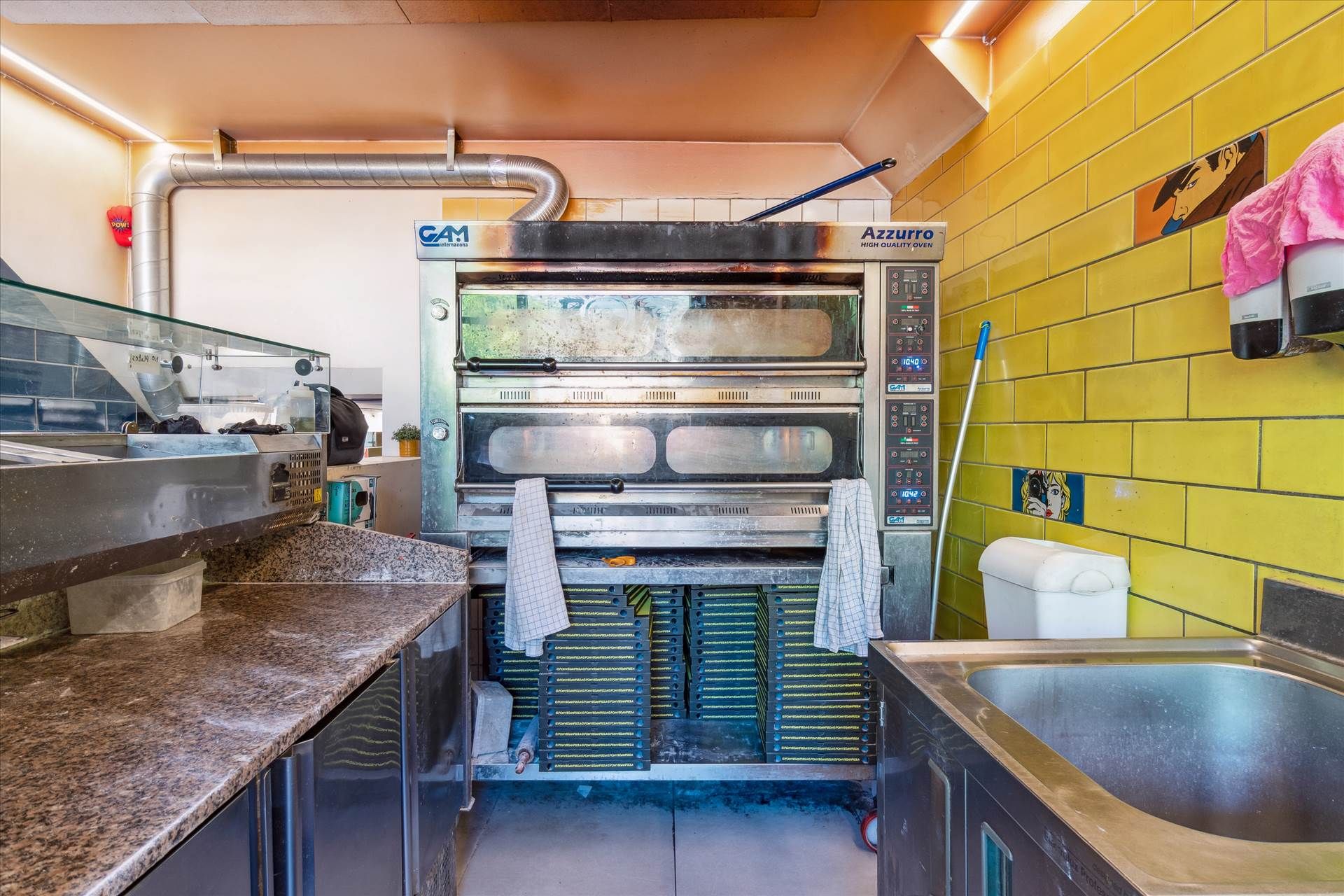 Et eksklusivt lejemål med kommerciel pizzaovn og et renseri. Ovenfor ovnen hænger et håndklæde og der er en vaskemaskine med