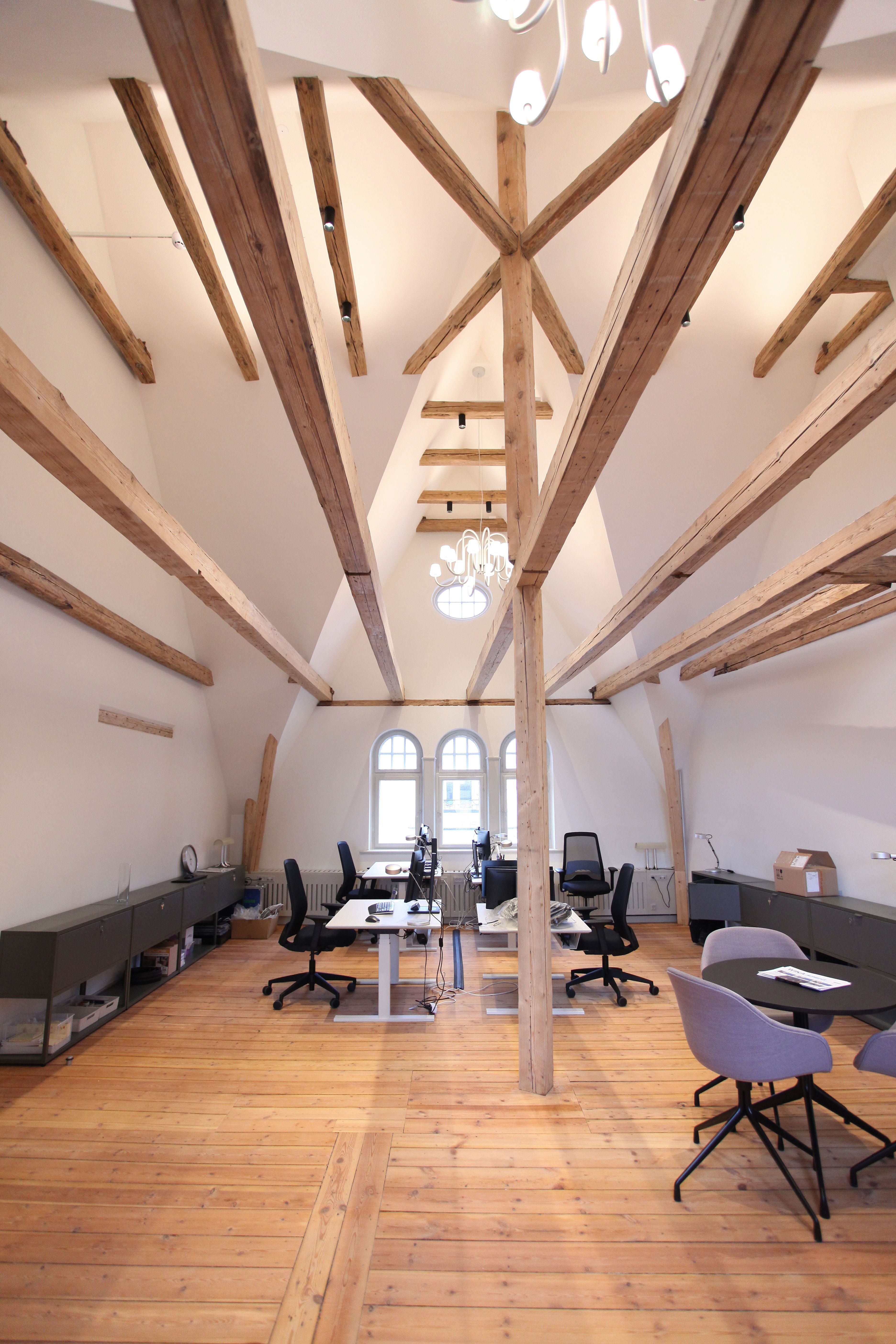 Træbjælker og loftsvinduer i et moderne kontor med højt loft og lyse gulve