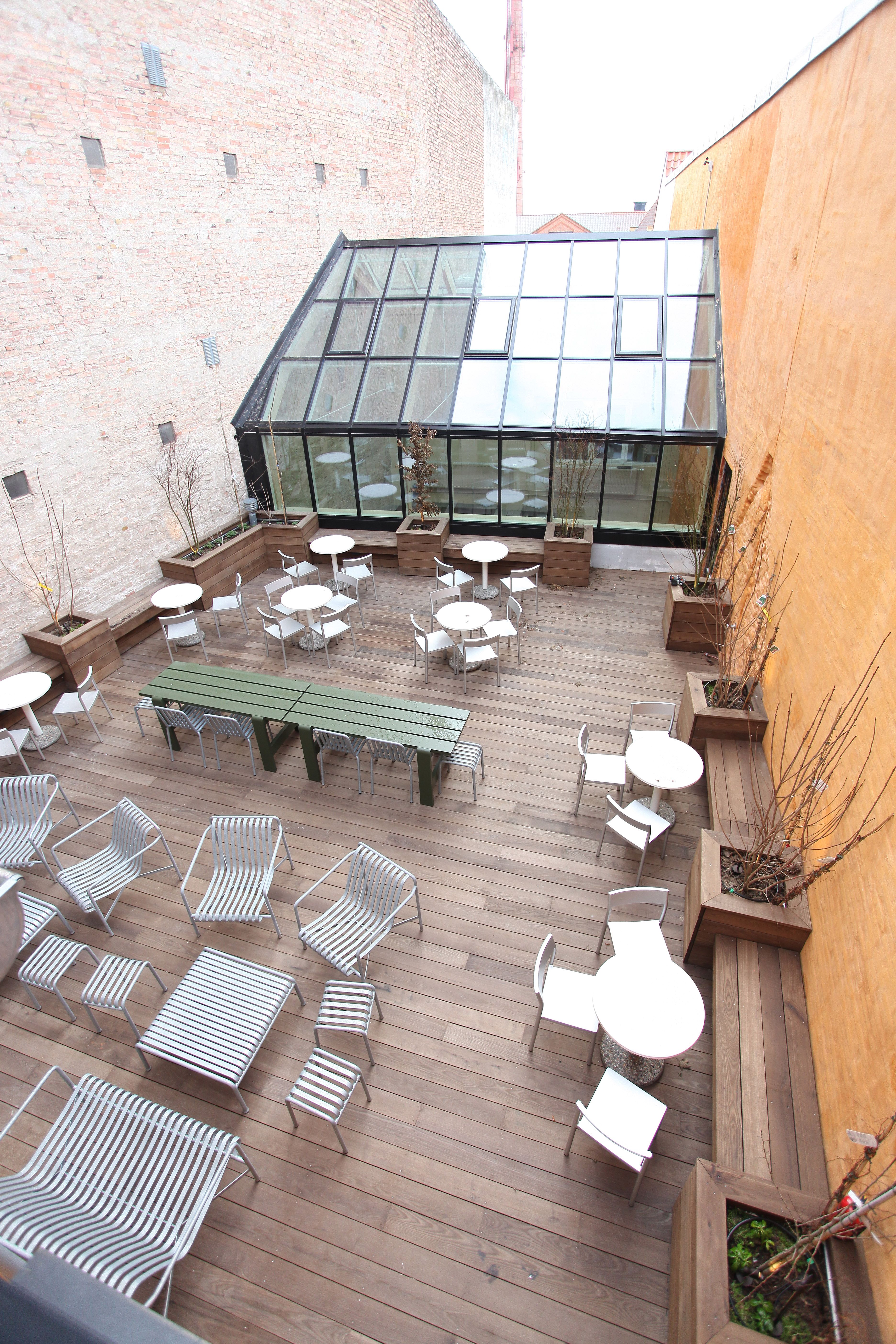 Lysskur og terrasse med borde og stole samt plantekasser i et kontorområde