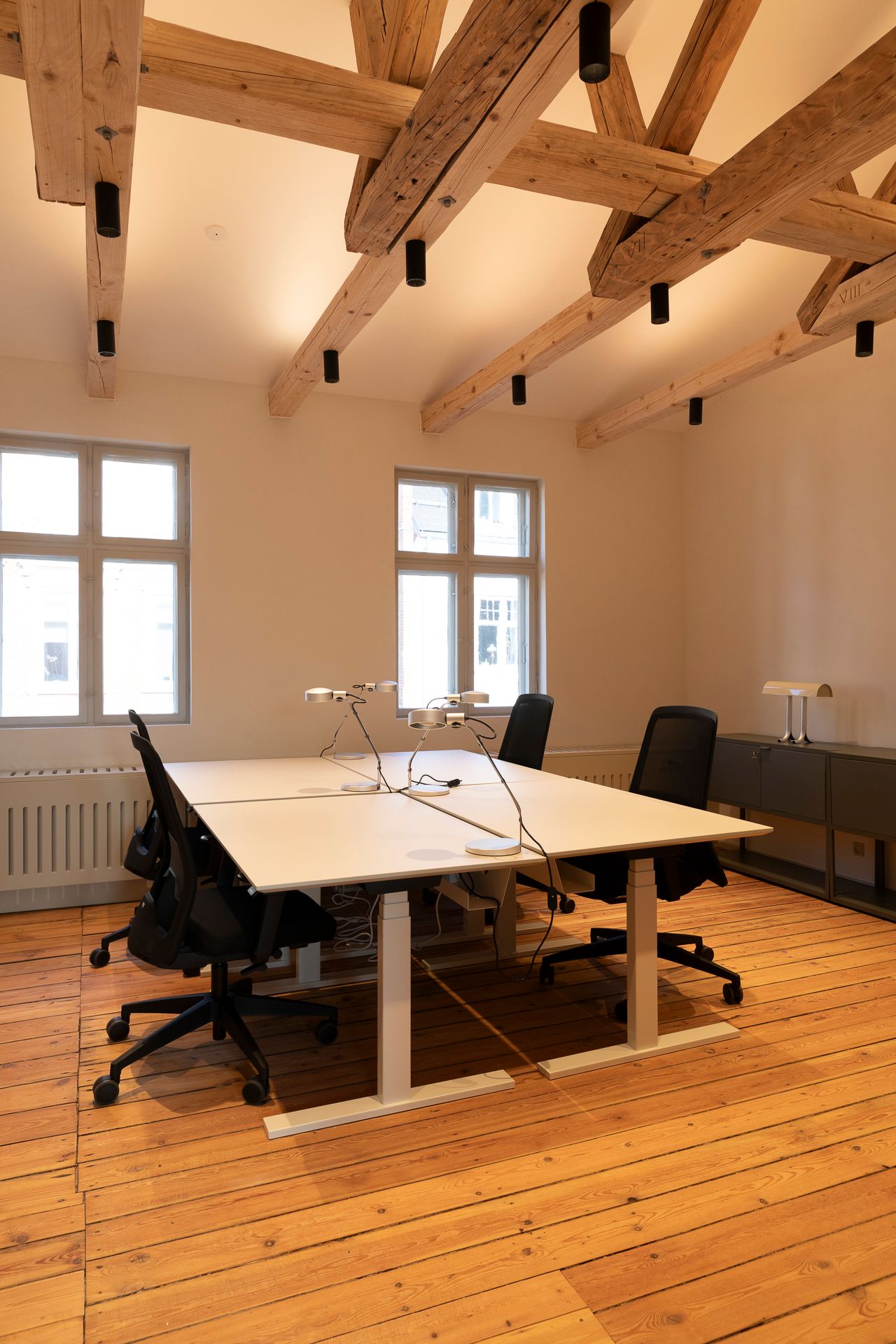 Kontor med lyse trægulve, tre borde og lyse blyantbøjle lysekroner hængende fra loftet
