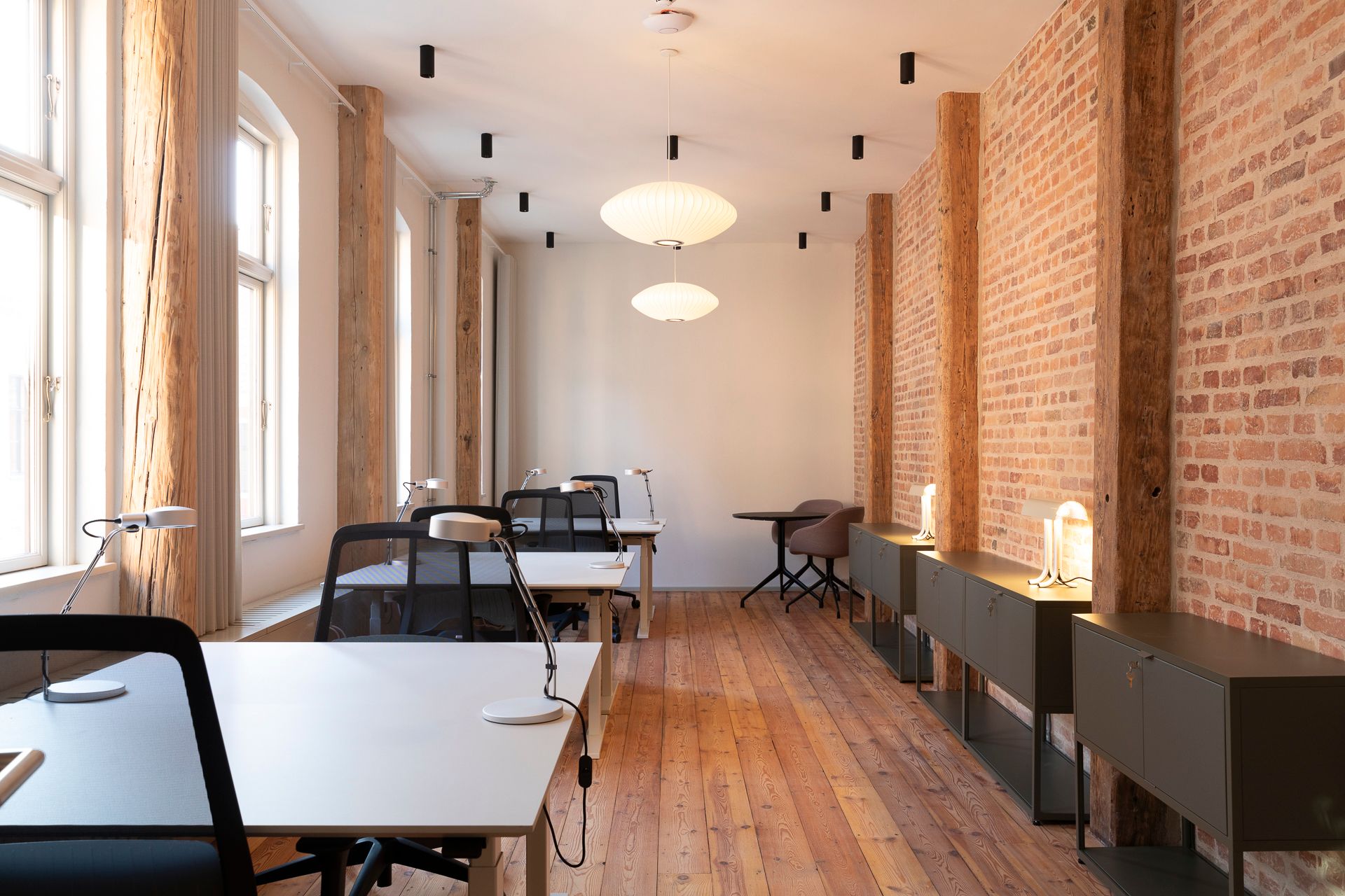 Kontor med lyse gulve, lyse lofter, lyse loftslamper og lyse møbler, hvor der er plads til flere skriveborde og stole.