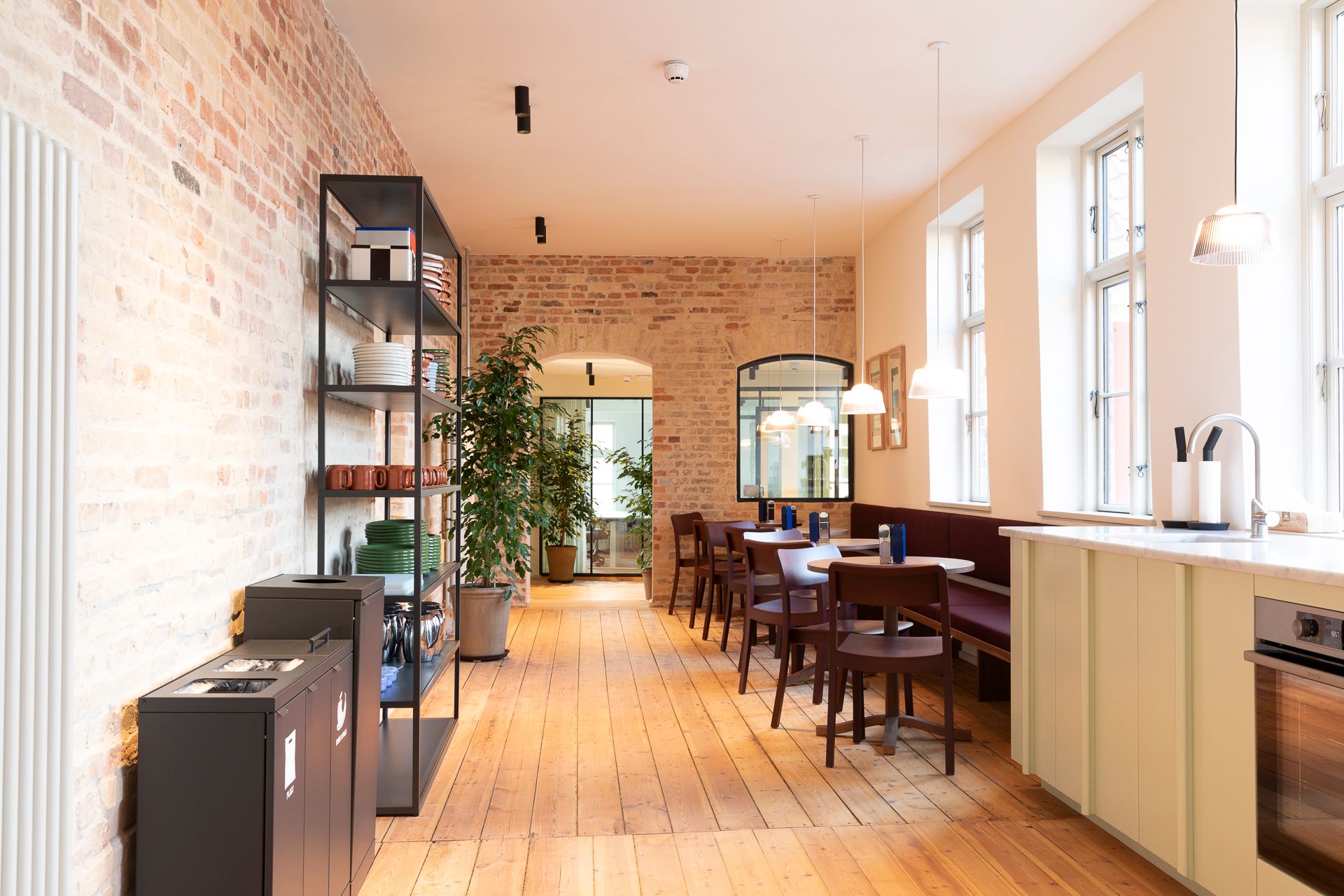 En hyggeligt indrettet restaurant med lyse trægulve, en lang mur af røde mursten og masser af grønne planter