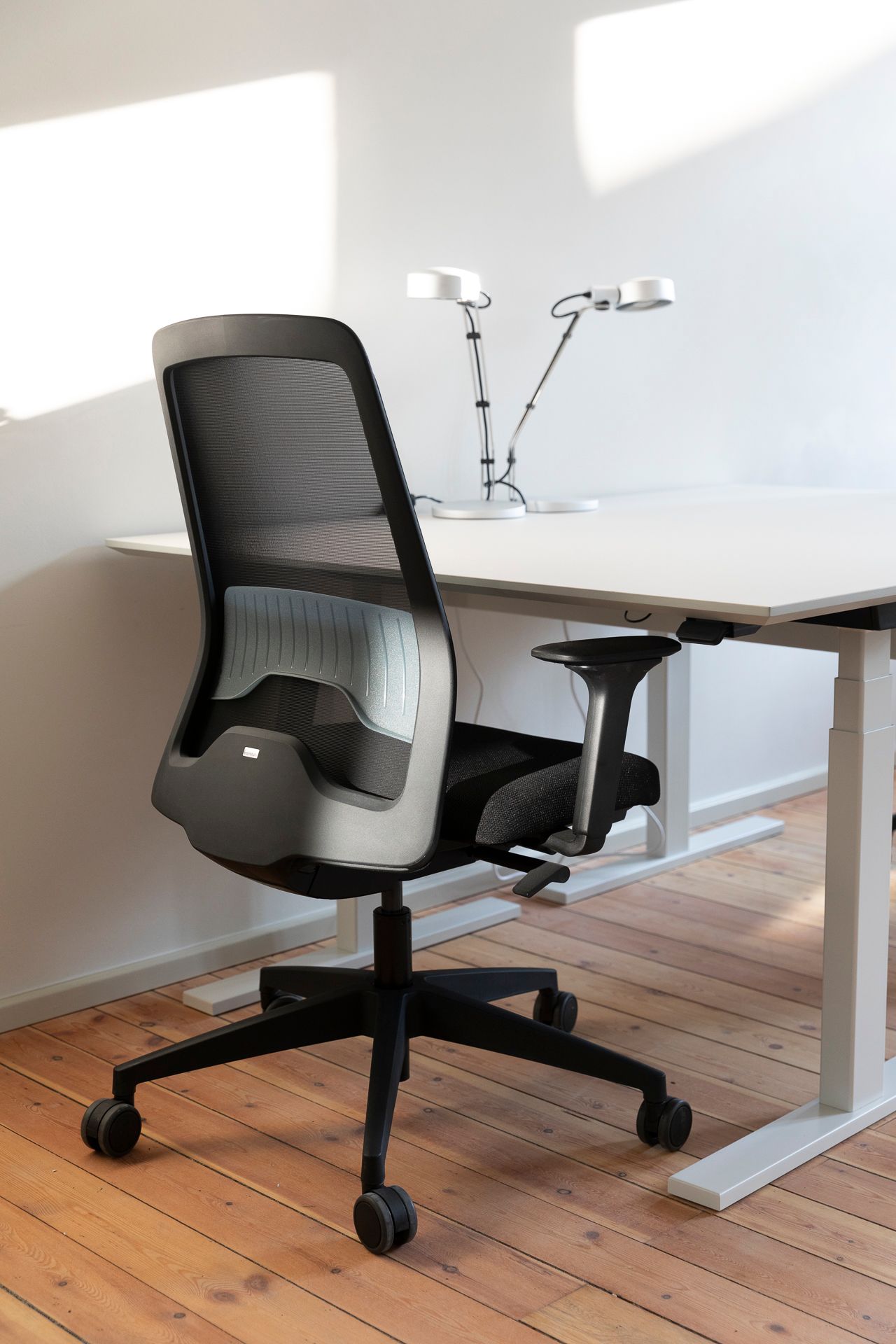 Moderne kontor stol med armlæn i sort og hvid med mesh ryglæn og hjul. Høj kontor bord med to hvide bordben og to hvide