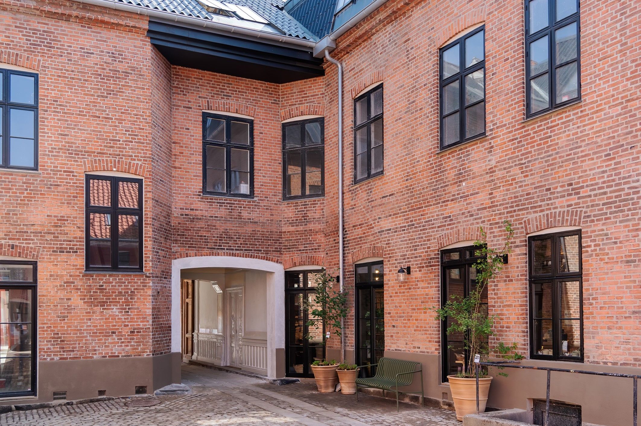 En lille gårdhave med røde mursten og et grønt sofabord, to plantepotter og en lysskilde