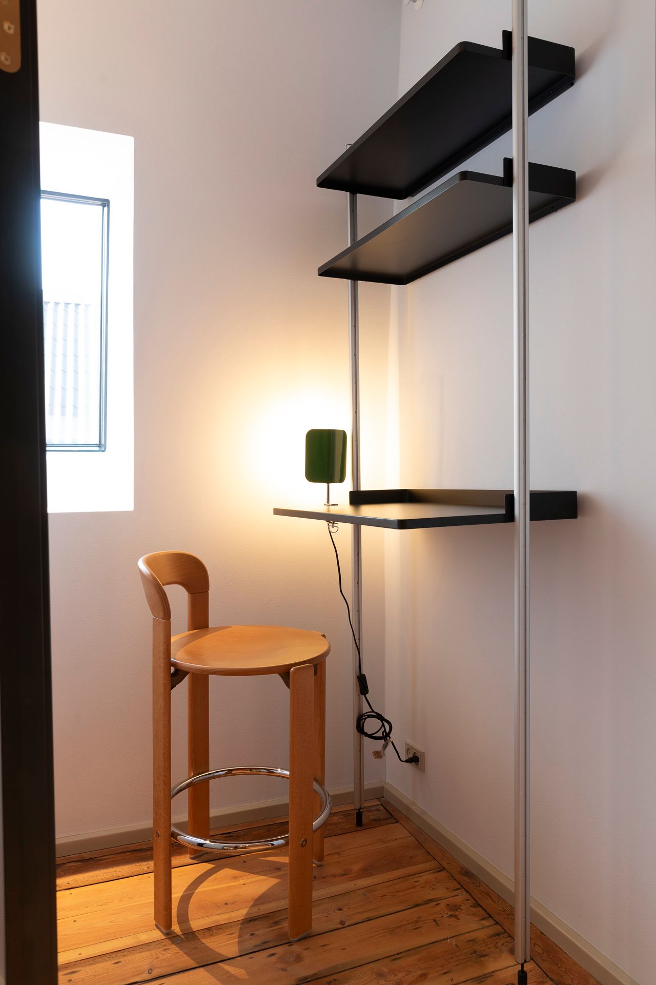 Lyst og funktionelt kontor med lysegul væg og høj stativ med to hylder og grønt bordlampe, hvor der er en lysegrå stol med