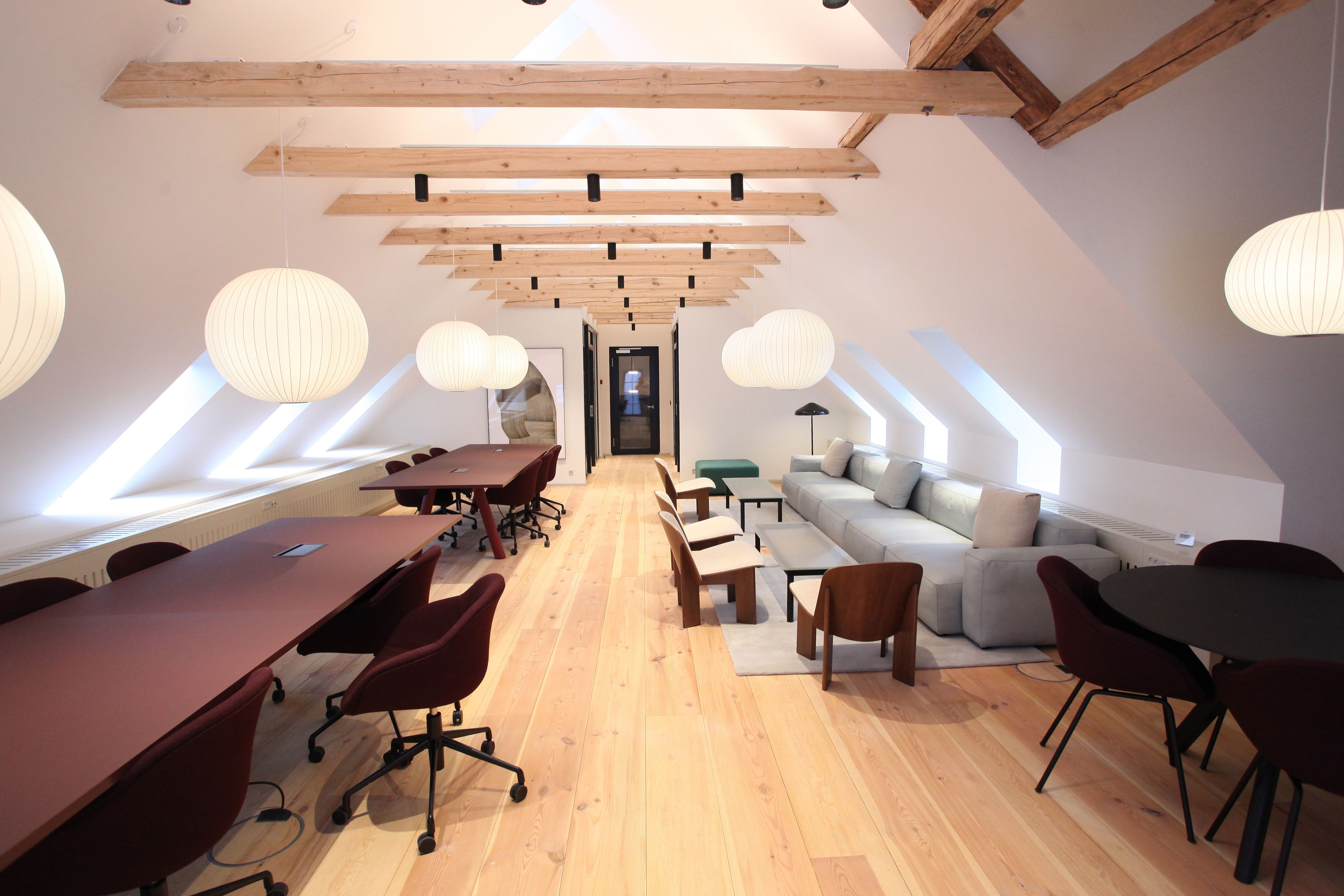 Kontor med lyse loftsbjælke, møbler og borde samt runde lysekroner. Der er en sofa, en sofabord og en lampe i enden af rummet