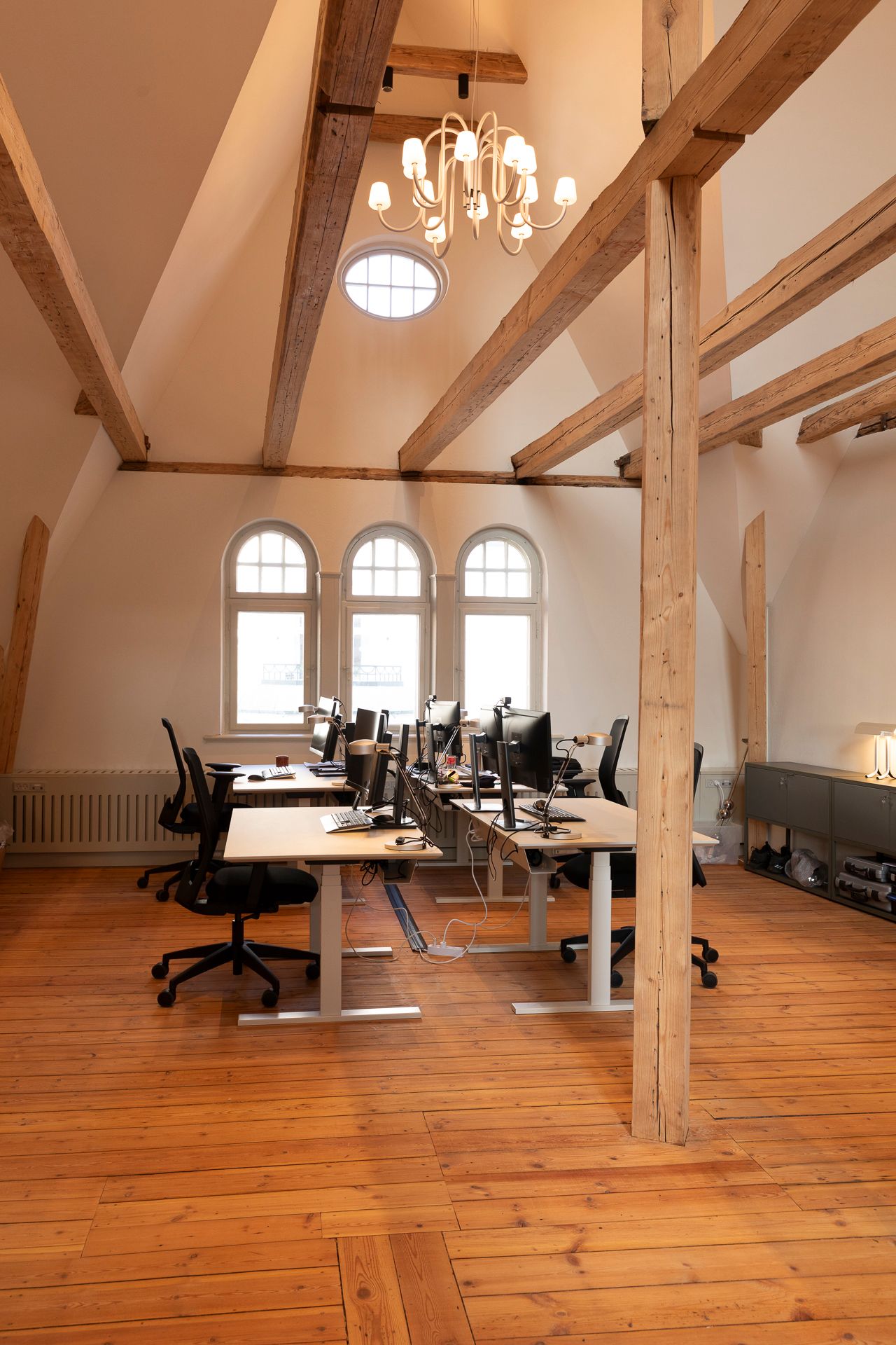 Inde i kontor med trægulve og træbjælker på loftet og runde vinduer med solskinsstråler trænger igennem