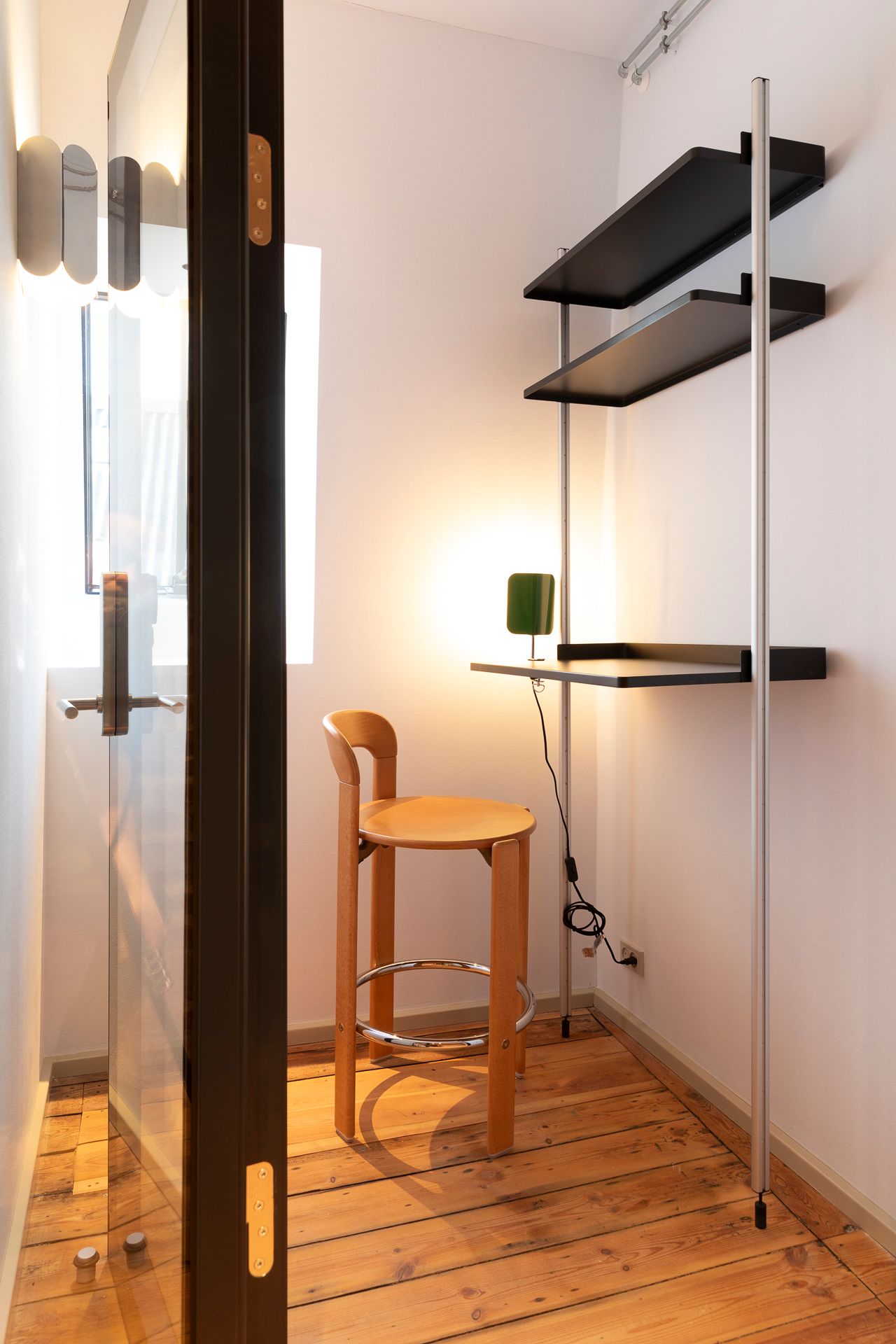 En høj børstol med gult sæde og metalfod. Et lille bord med gulvtæppe. En simpel hylde med to sorte hylder. En stol uden