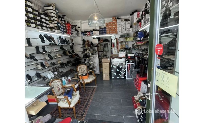 Butik med mange sko på hylder og gulvet, møbler og kasser med sko og etiketter, åbent glasdør og et gulv med tæpper og en