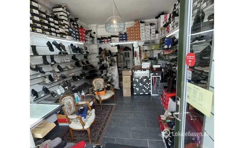 Butik med mange sko på hylder og gulvet, møbler og kasser med sko og etiketter, åbent glasdør og et gulv med tæpper og en