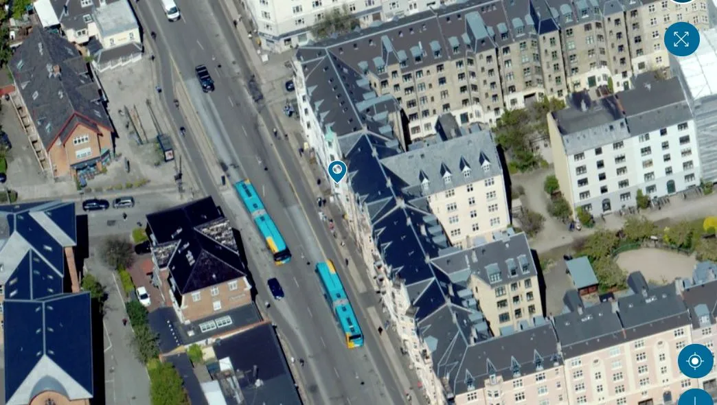 Luftfoto af en by med mange huse og gader, to busser kører på en bred gade, vejen er fyldt med biler og folk, der går på