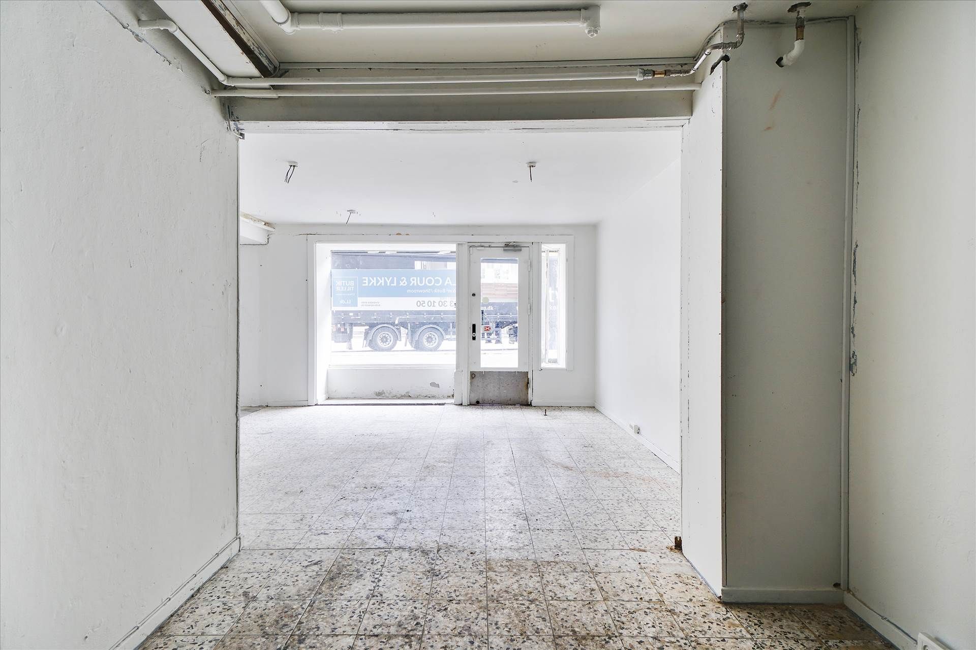 Tomsgårdsvej og Frederiksborgvej krydses af en lastbil. Udlejes erhvervslokaler med en glasdør og et vinduesparti.