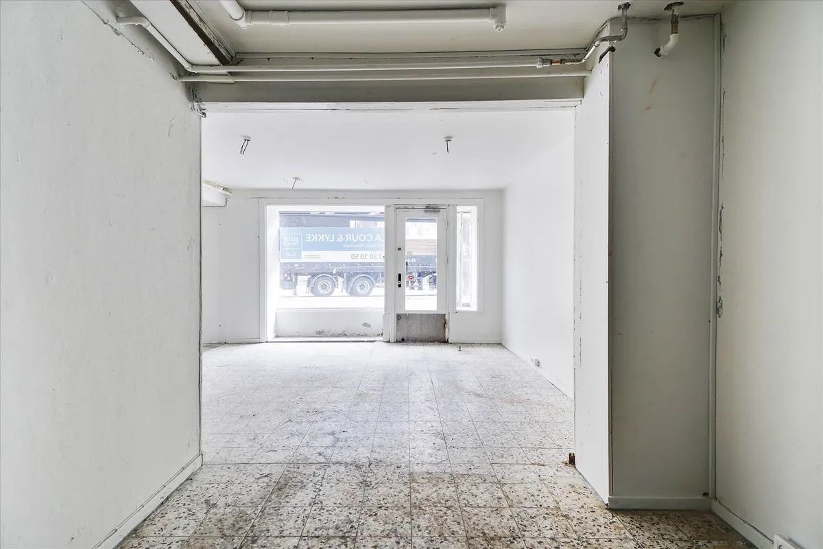 Tomsgårdsvej og Frederiksborgvej krydses af en lastbil. Udlejes erhvervslokaler med en glasdør og et vinduesparti.