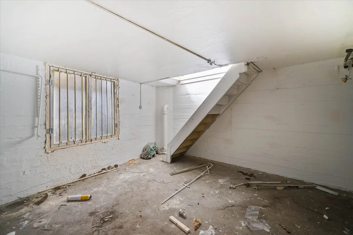 En ubenyttet lagerrum med en trappe og et vindue, samt forskellige smadrede genstande og affald på gulvet