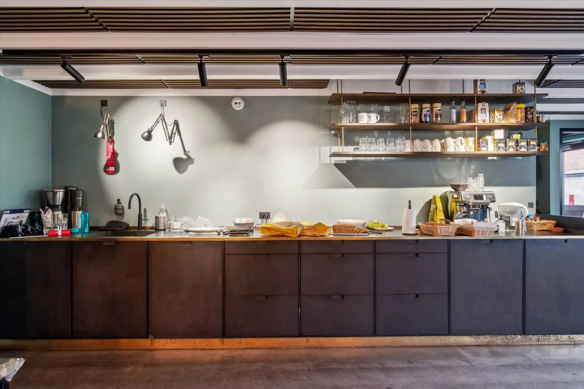 Stilfuldt køkken med møbler i sort og brun, lysekroner og loftsbælte i brunt, hylder med glas og tøj, og en kaffemaskine og