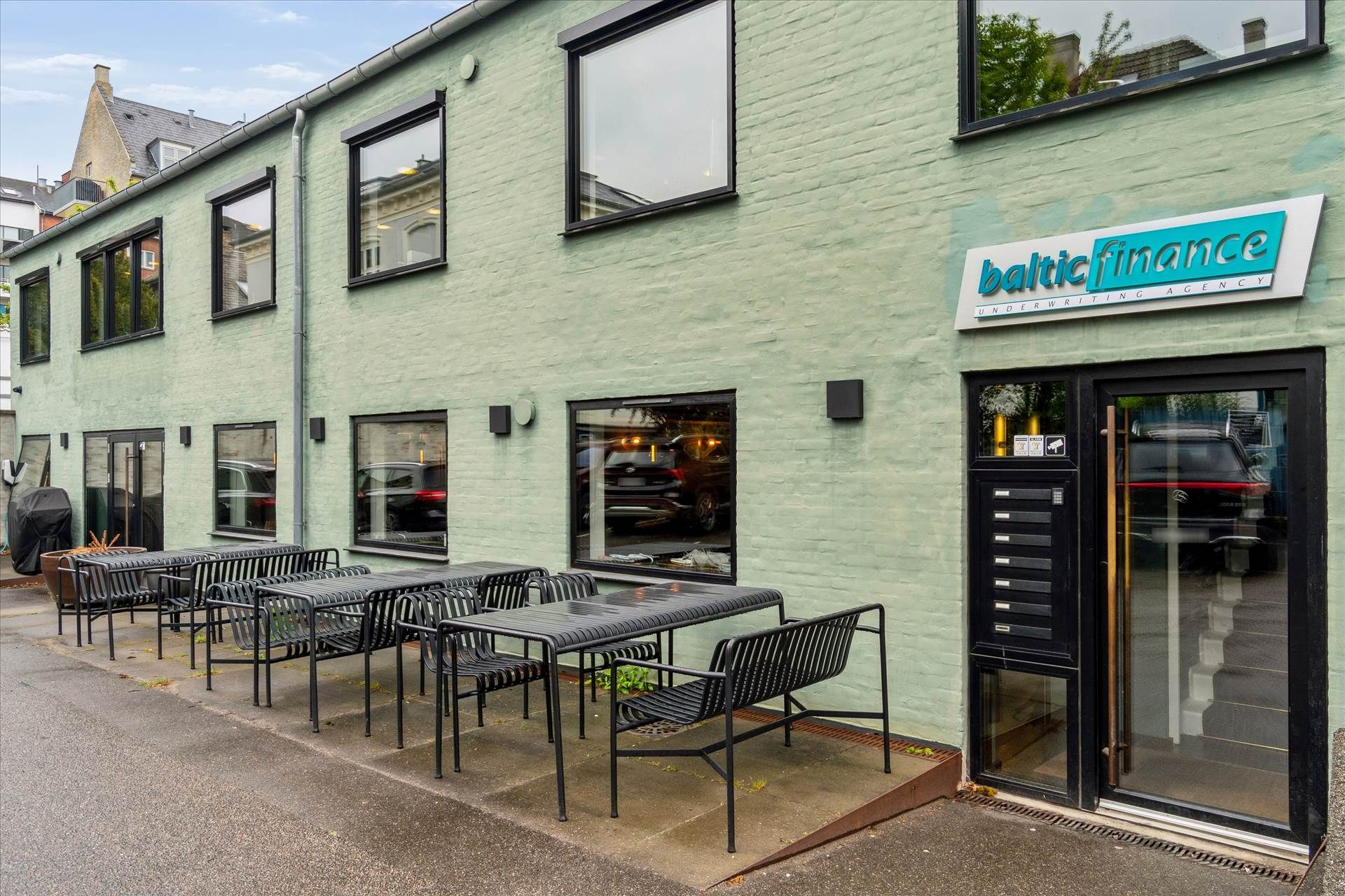 Kontor i baghus med havemøbler og glasdøre samt vinduer og skilte med teksten Baltic Finance Underwriting Agency