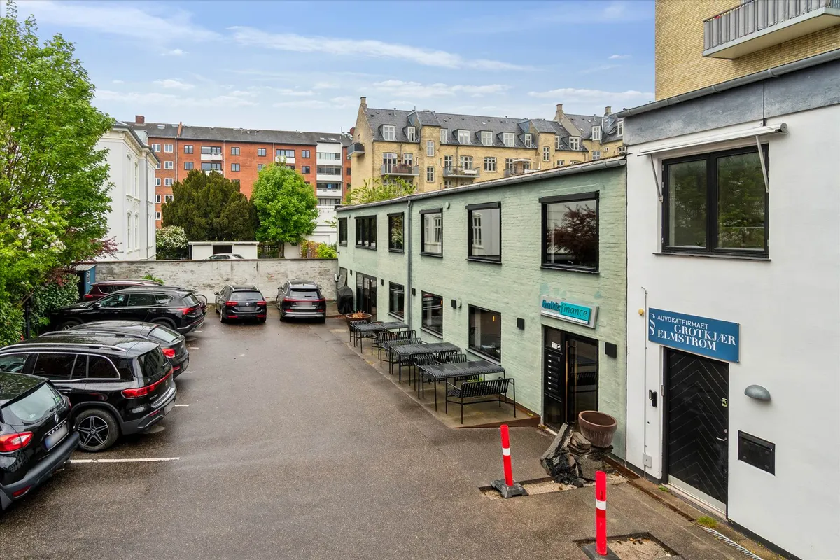 Baghus med parkeringsplads og kontorer og møbelfirmaer. Der er parkeret biler og grønne plantager.