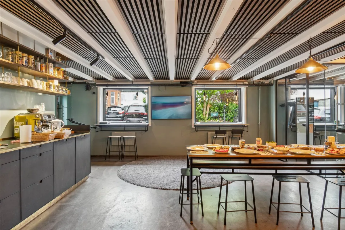 Hyggeligt køkken med lyse loftsbjælker og lysekroner, køkkenudstyr og retter på bordet, gulvtæppe og stole, vindue med