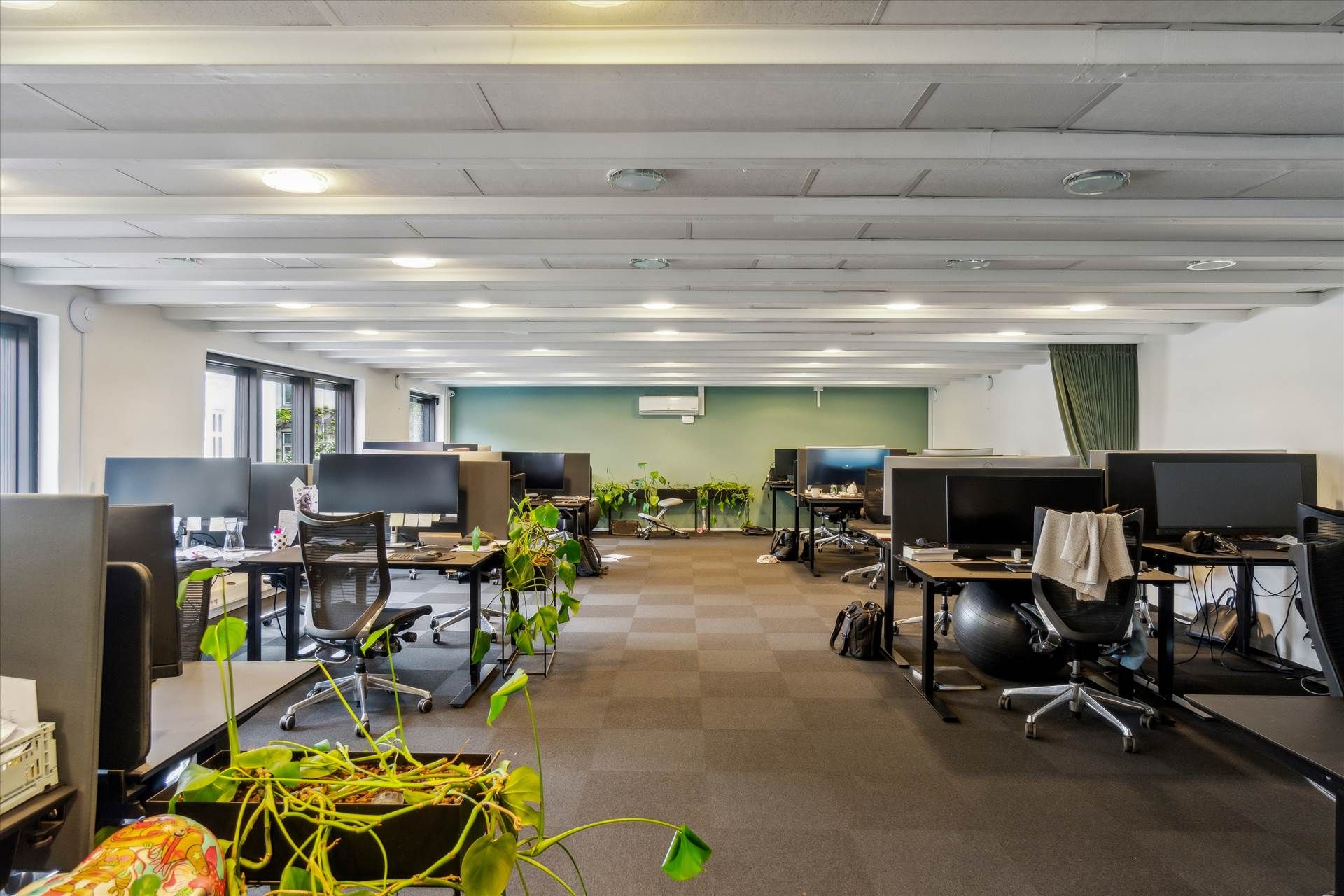 En række kontormøbler og computere står stille på et kontorlokal med hvide vægge og lyse loftsbjælker