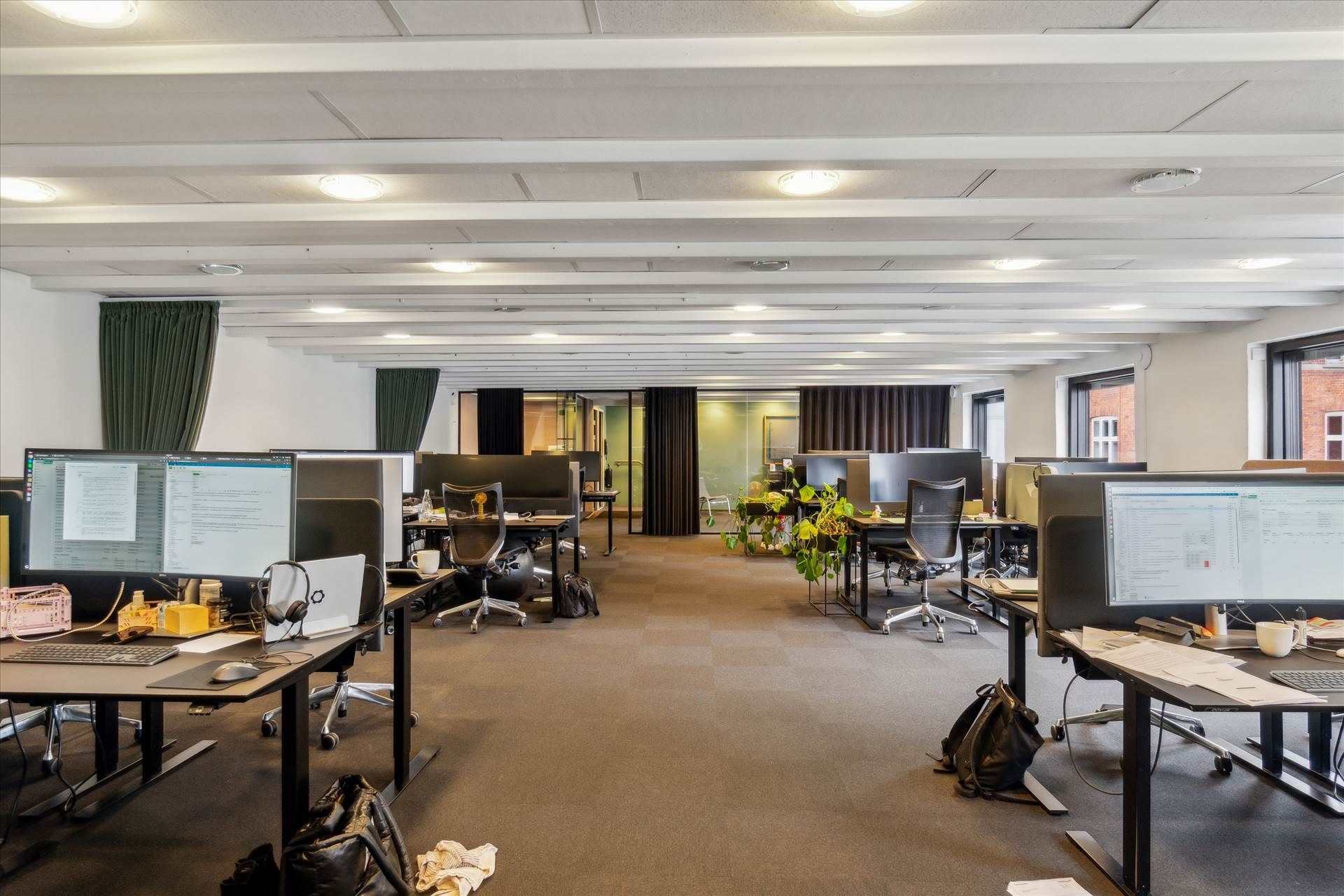 Moderne kontor med flere skriveborde, computere, højtalere, kuffert og stol. Komplet indretning med tavler og møbler.