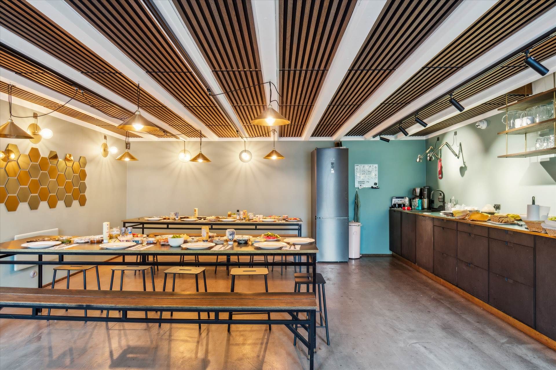 Bord med frokostmad i stue med højt loft, møbler og hvide vægge samt gulv og køleskab med apparater og tekstiler