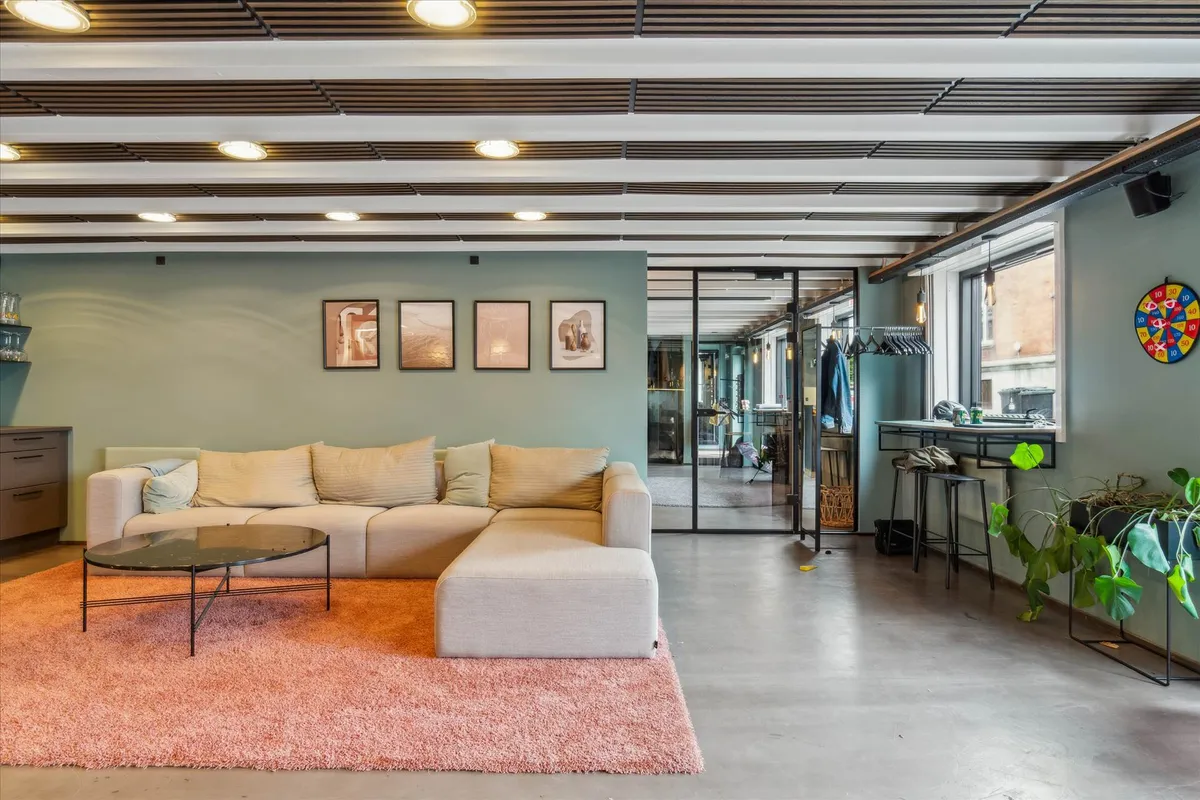 Stilfuldt kontor med sofa, kaffebord, plante og tre kunstværker i lyse grønne vægge.