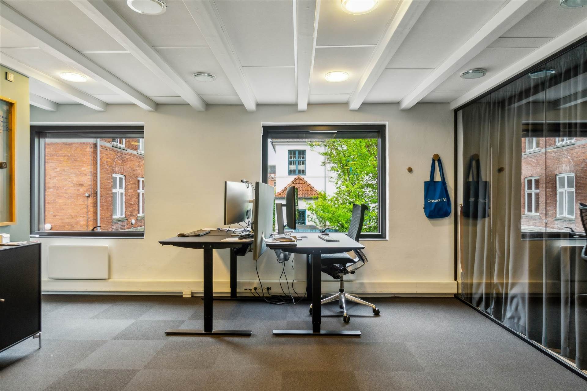 Moderne kontor med to skriveborde og to computere, møbler og tekstiler i sort og blå, vinduer med udsigt til gaden og