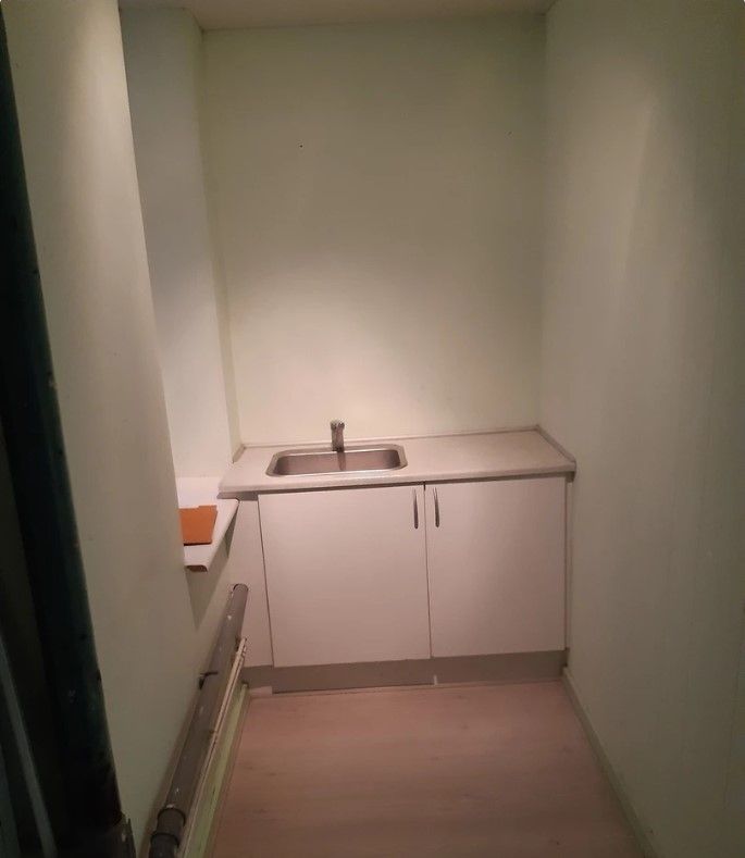 Et lille køkken med hvidt bord og to hængeskabe, der er lukket og en åben dør