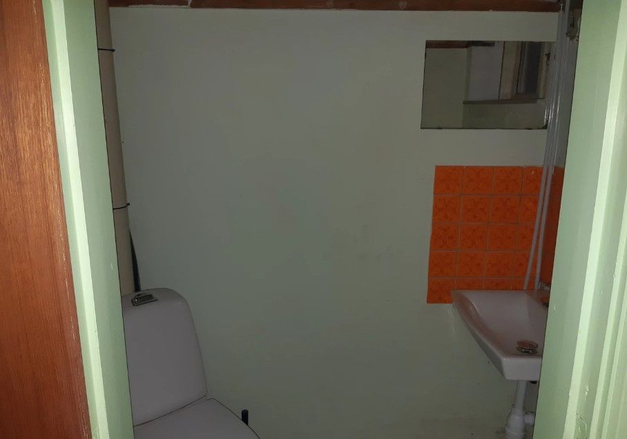 Toilette med hvid toiletkasse og hvidt vask i en lille rummelig toiletrum med orange fliser og spejl i væggen