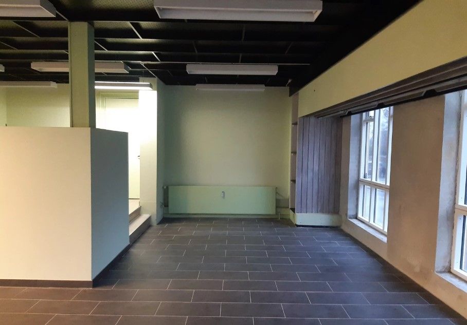 Kontor med åbent rum, blankgulv, lysegul væg og en gul-blå sektion med trapper og lyse glasdøre