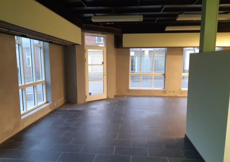 En tom og klar stue med store vinduer og højt til loftet. Gulvet er lige og mørkt og der er adgangsdøre i midten.