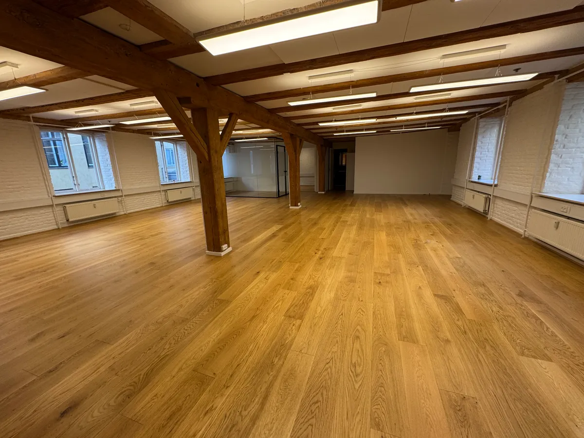 En stor, tom lejlighed med lyse trægulve og lyse hvide vægge med flere vinduer og lysekroner på loftet