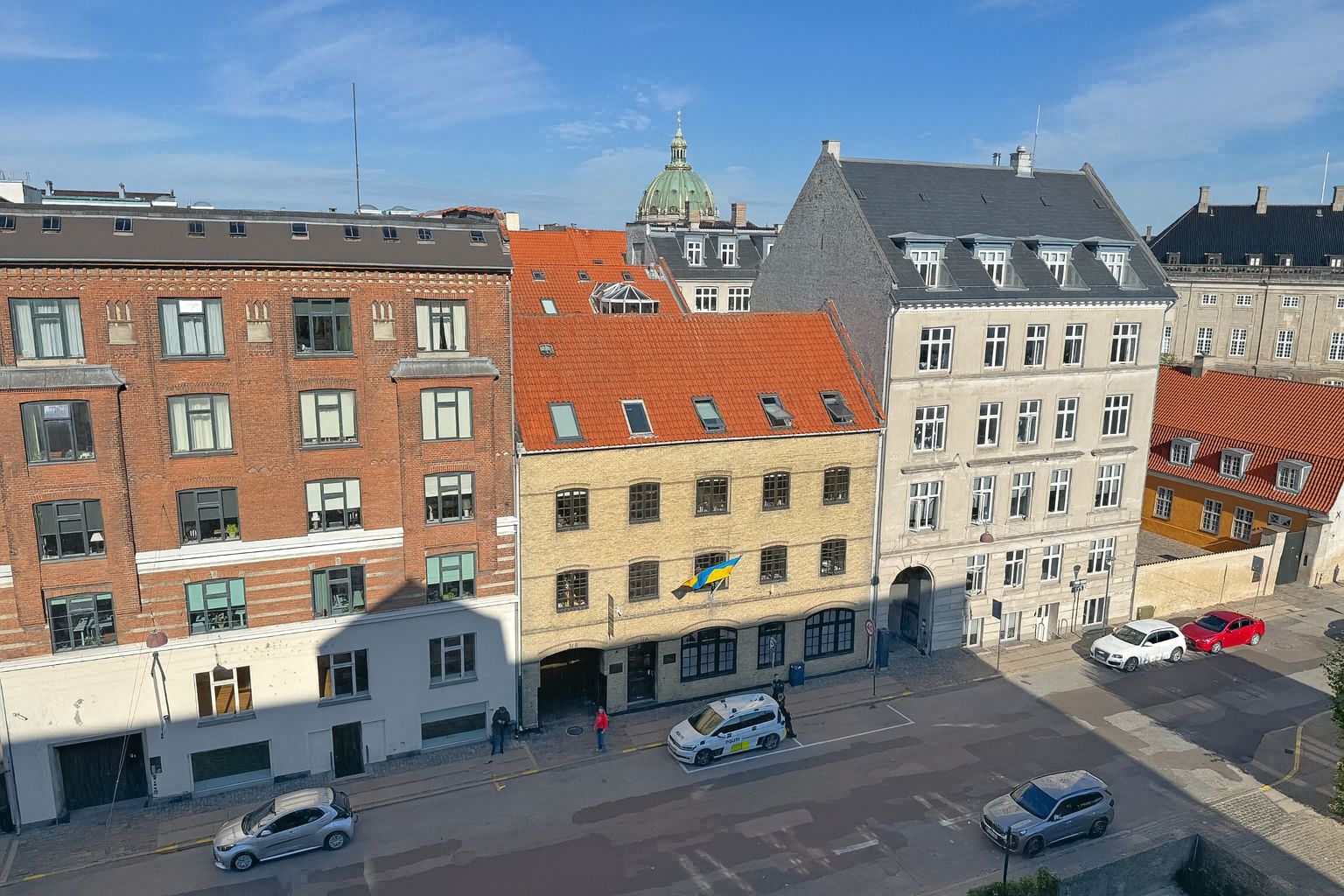 Forsiden af Toldbodgade 37 B med en politibil parkeret foran bygningen og folk stående ved indgangen