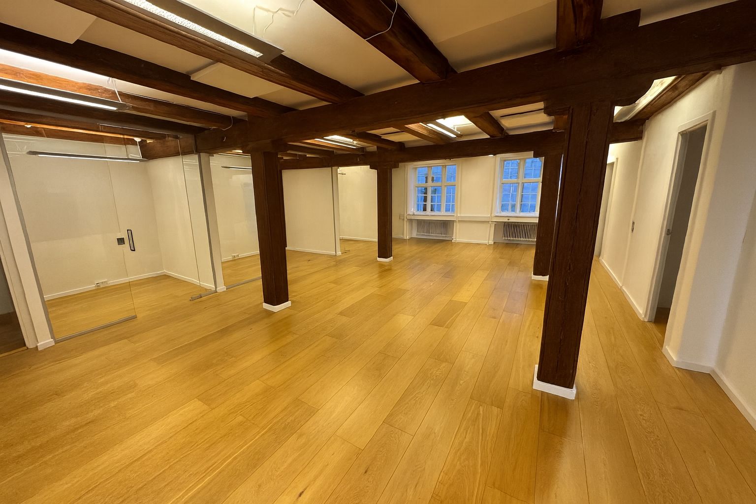 Lys, moderne kontorlokaler med trægulv og store ruder med udsigt til byen. Loftet er udstyret med lysekroner og træbjælker.