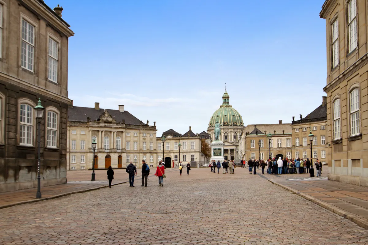 Folk går i Frederiksstaden med Charlottenborg og Amalienborg i baggrunden, og der er en statue foran Charlottenborg