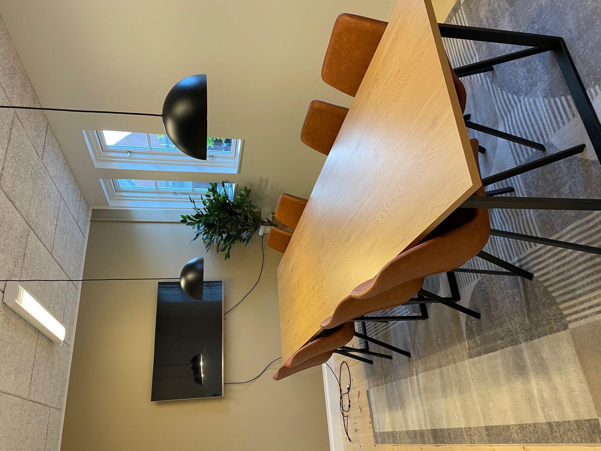 Moderne mødebord i en historisk banegård med fire læderstole og to moderne lampekroner