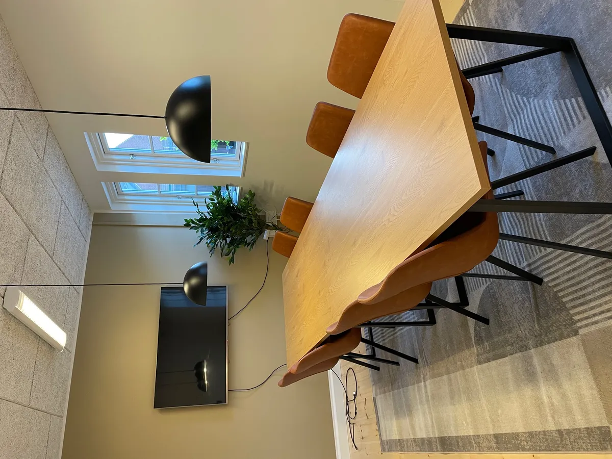 Moderne mødebord i en historisk banegård med fire læderstole og to moderne lampekroner