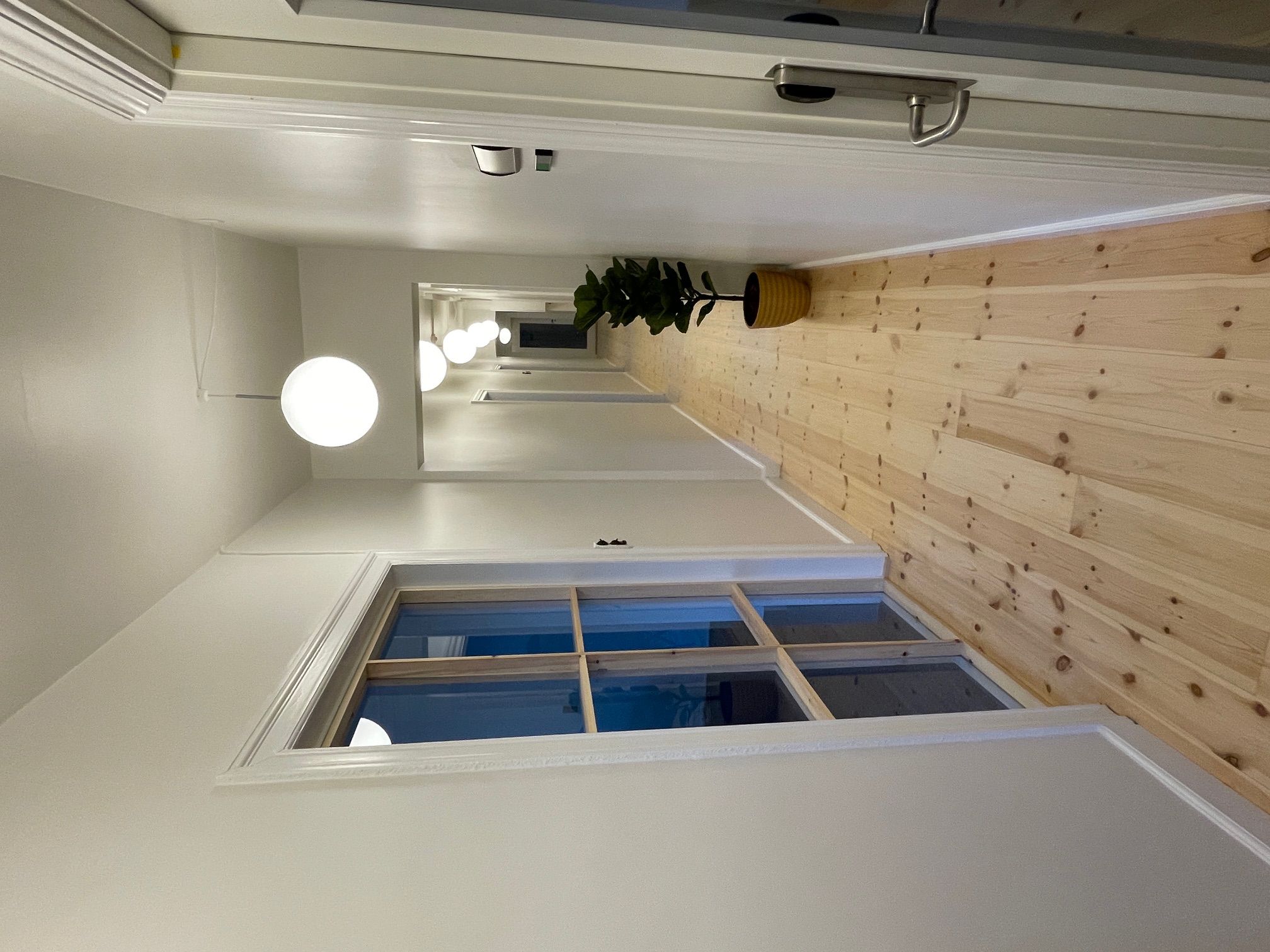 Lys, åbent kontor med hvide vægge og lysegule lofter. Lyskroner med kugleformede lamper. Gulvbelægning af lysebrunt træ.