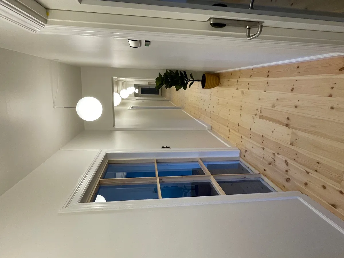 Lys, åbent kontor med hvide vægge og lysegule lofter. Lyskroner med kugleformede lamper. Gulvbelægning af lysebrunt træ.