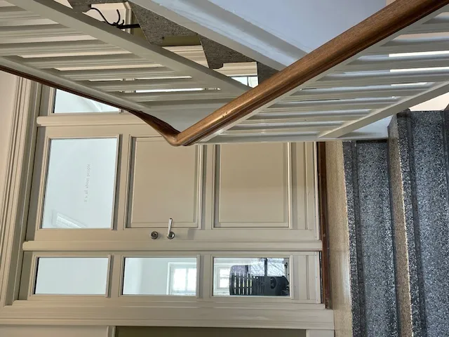 En hvid indgangsdør med tre glasruder og en slank håndtag i metal og træ stiger op mod et hvidt loft