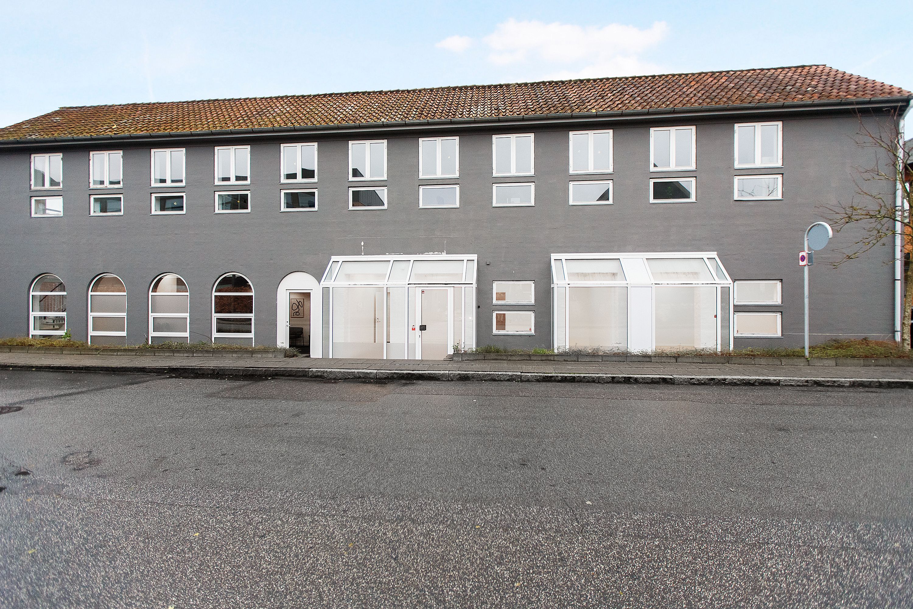 Moderne klinkfællesskab i Kolding med mange vinduer og hvide døre på en tom gade under en lyseblå himmel
