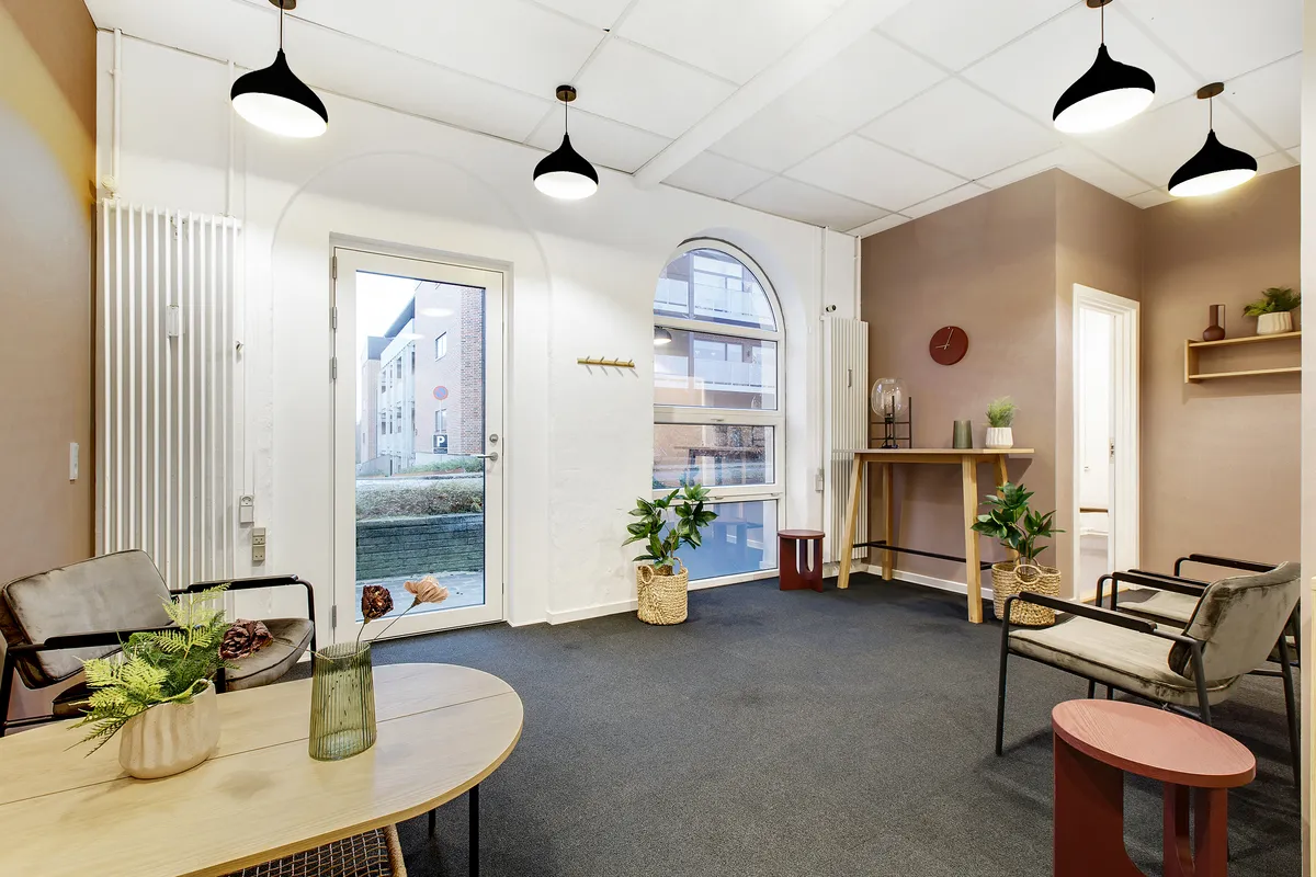 Klinkfællesskab i Kolding med plantepotter, lysekroner og en hvid dør til et værelse med et smil.