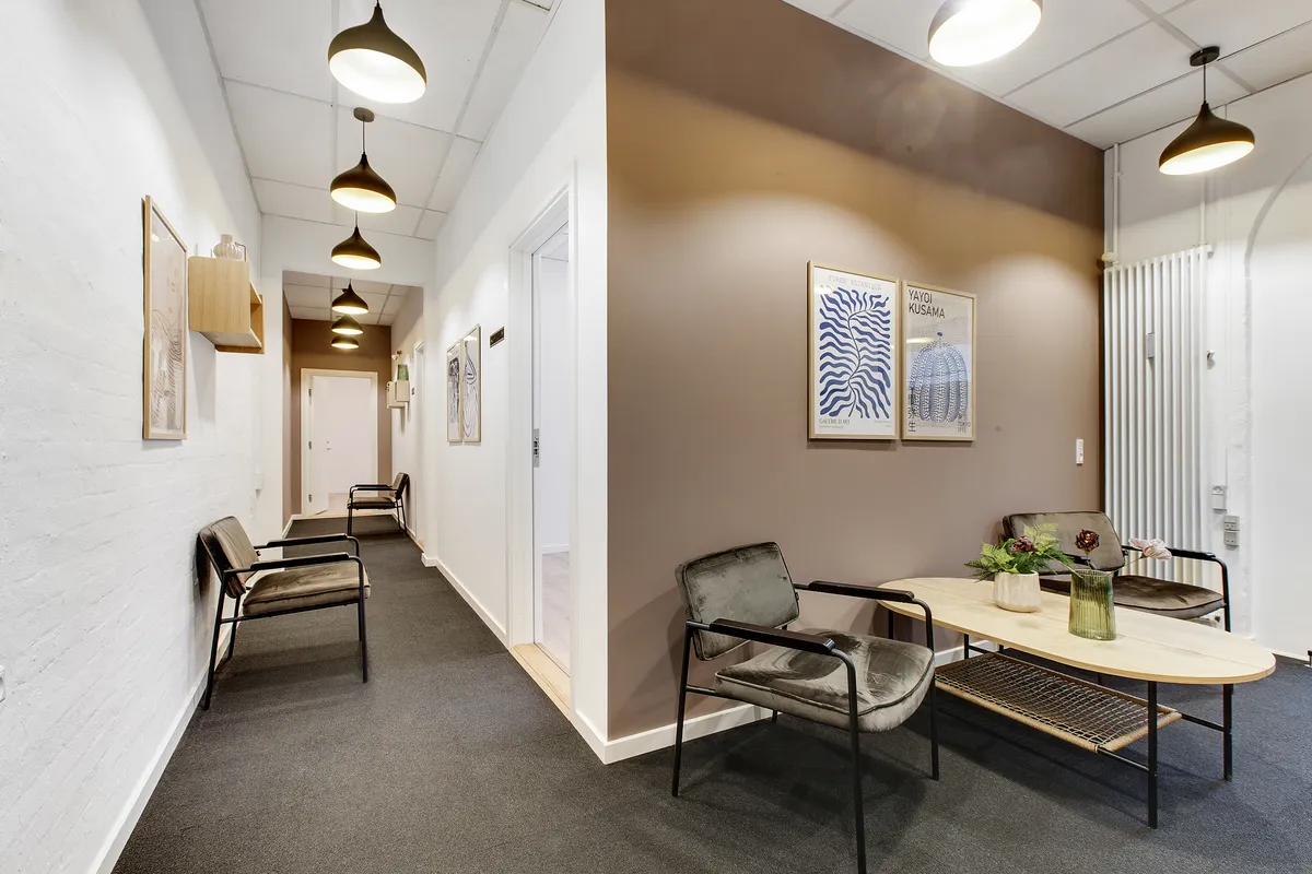 Indvendig hall med højt loft og lyse krydsfinergulve og møbler i lysebrune og grå nuancer og kunst på væggen