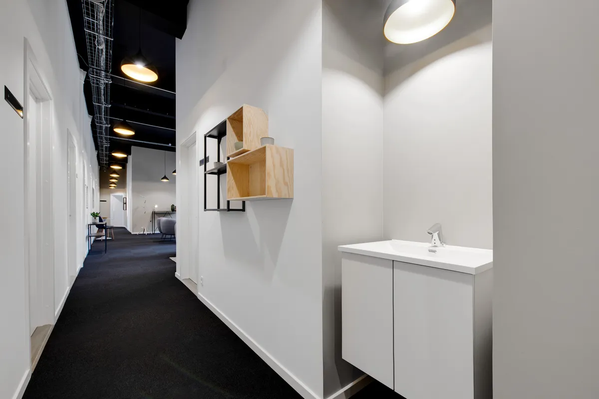 Et smal korridor med hvide vægge, gulv og loft, og møbler i minimalistisk stil, samt et toilet med hvid vask og lysekroner