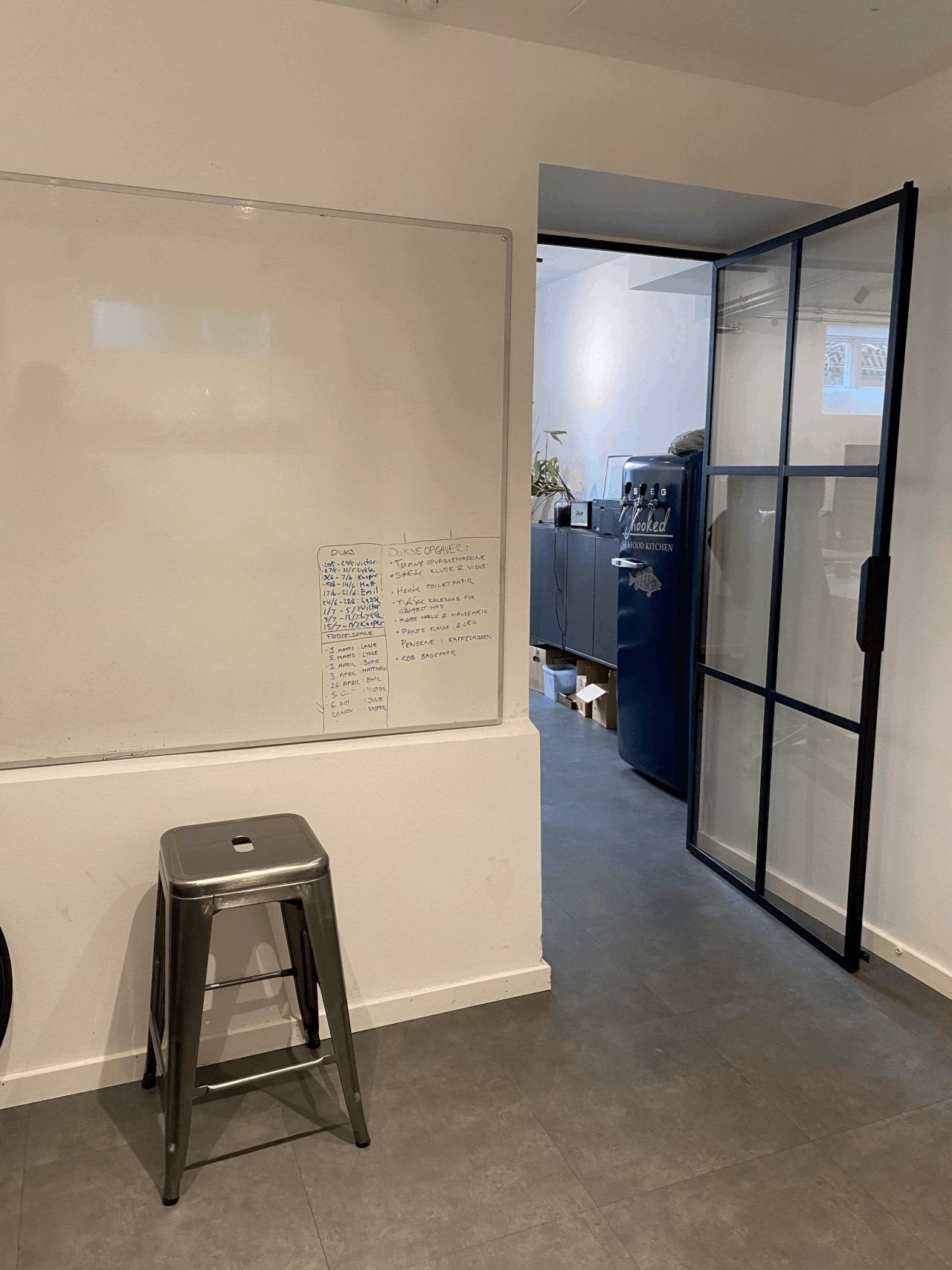 Høj kvalitet whiteboard med flere opgaver og tekster. Sort metal stol står mod væggen. Et stort glasdør står åbent og giver